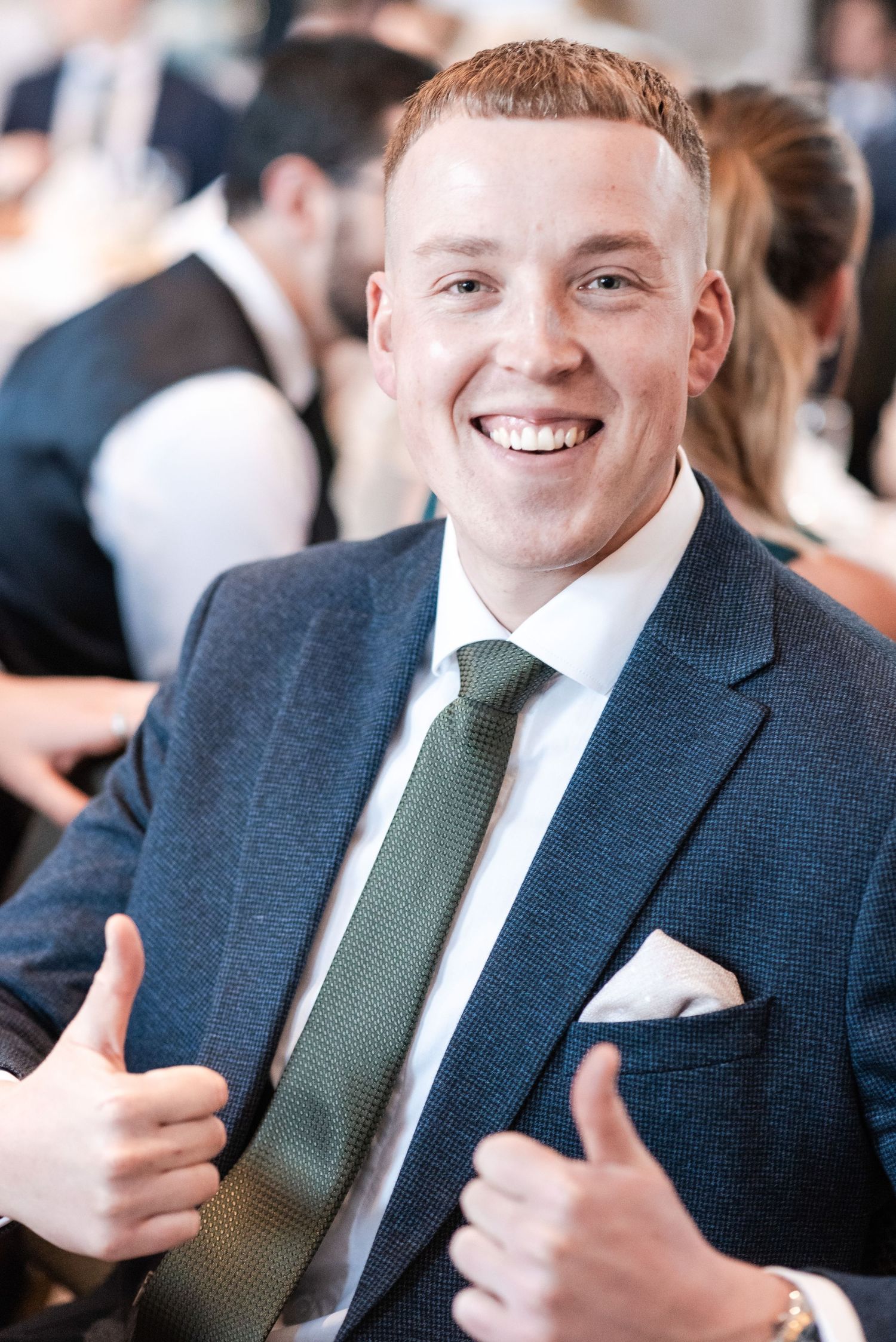 Professional wearing a navy suit and green tie gives thumbs up gestures in a sequence of candid office photos.
