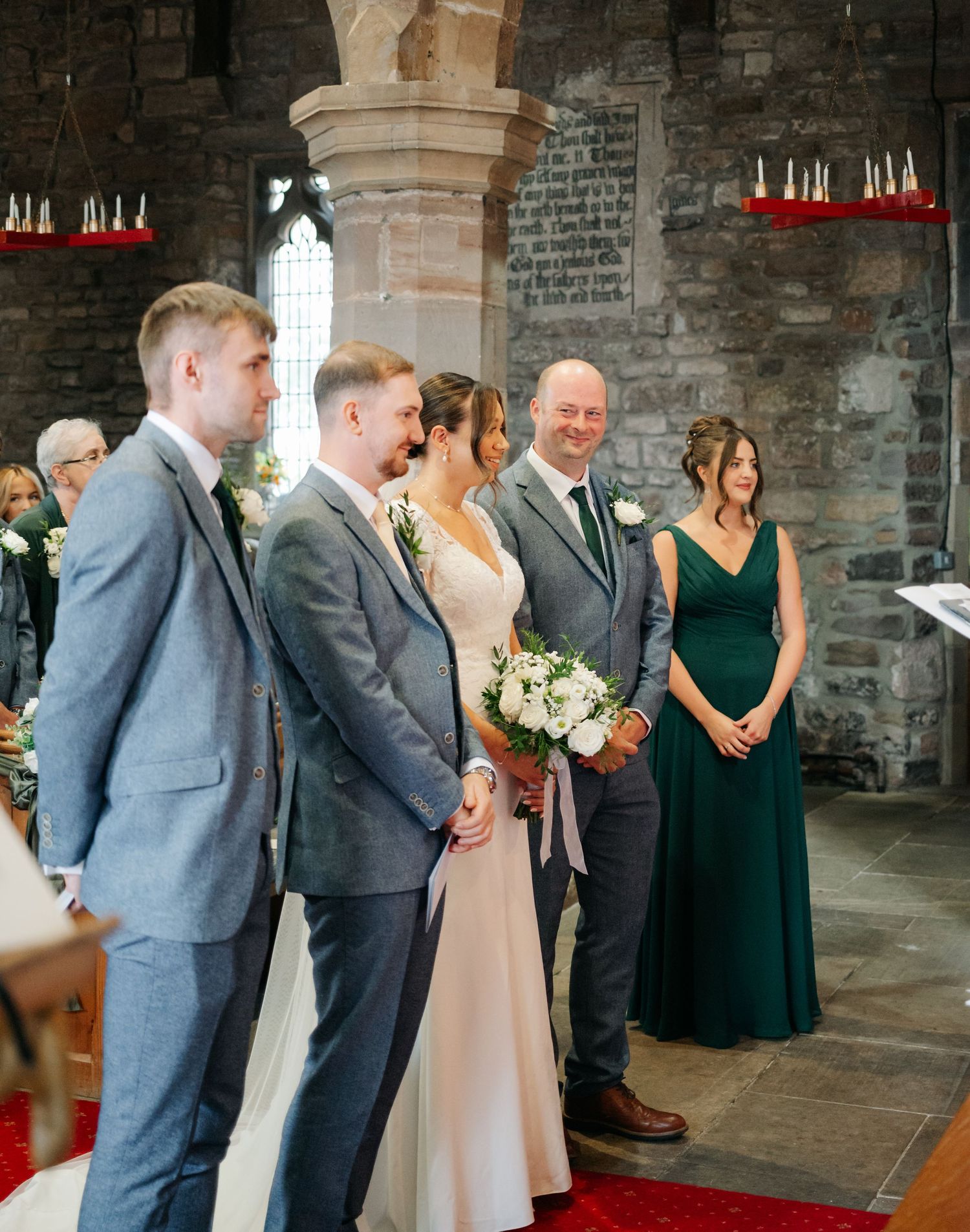 Wedding party members in gray suits and green dresses lined up during ceremony.