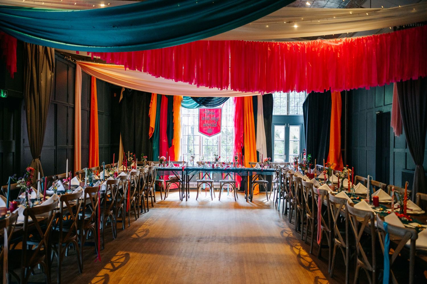 A wedding reception venue decorated with dramatic red and teal fabric draping and wooden chairs.