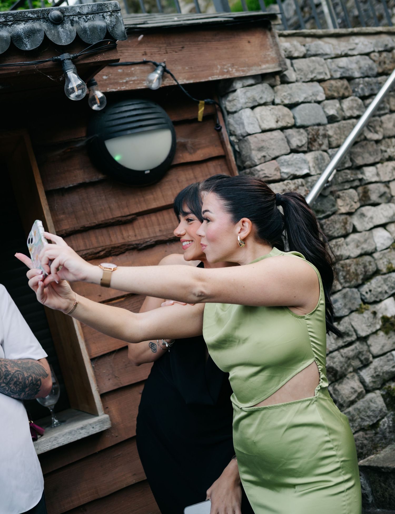 Wedding guests taking selfie photos outside rustic wooden structure.
