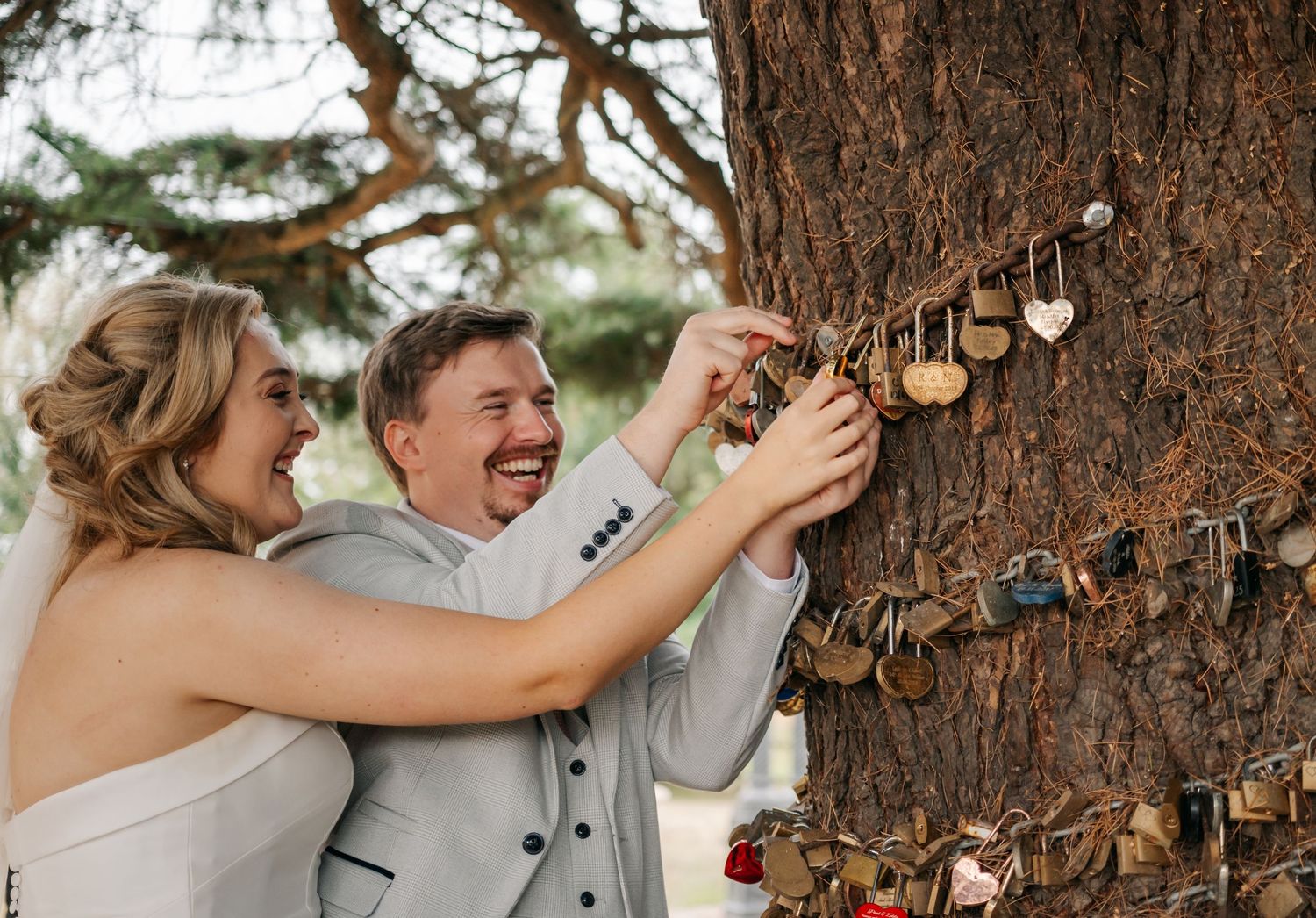 A couple laughs while interacting with decorative items hung on a large tree trunk.