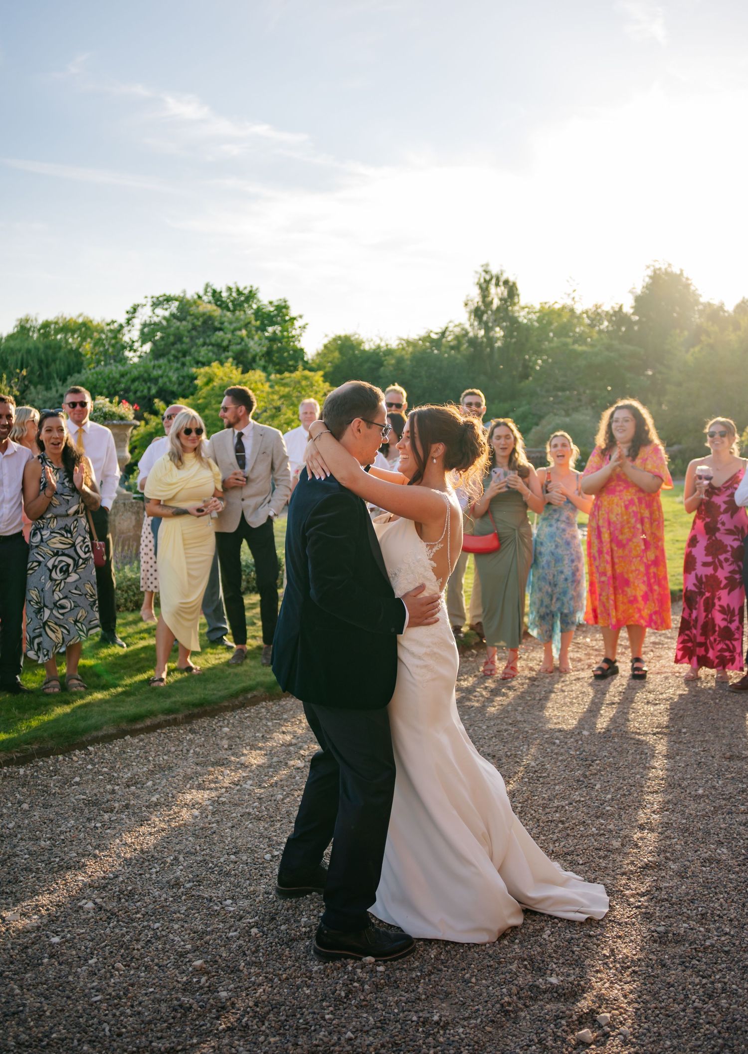 Wedding guests dance together on a gravel path during golden hour celebrations.