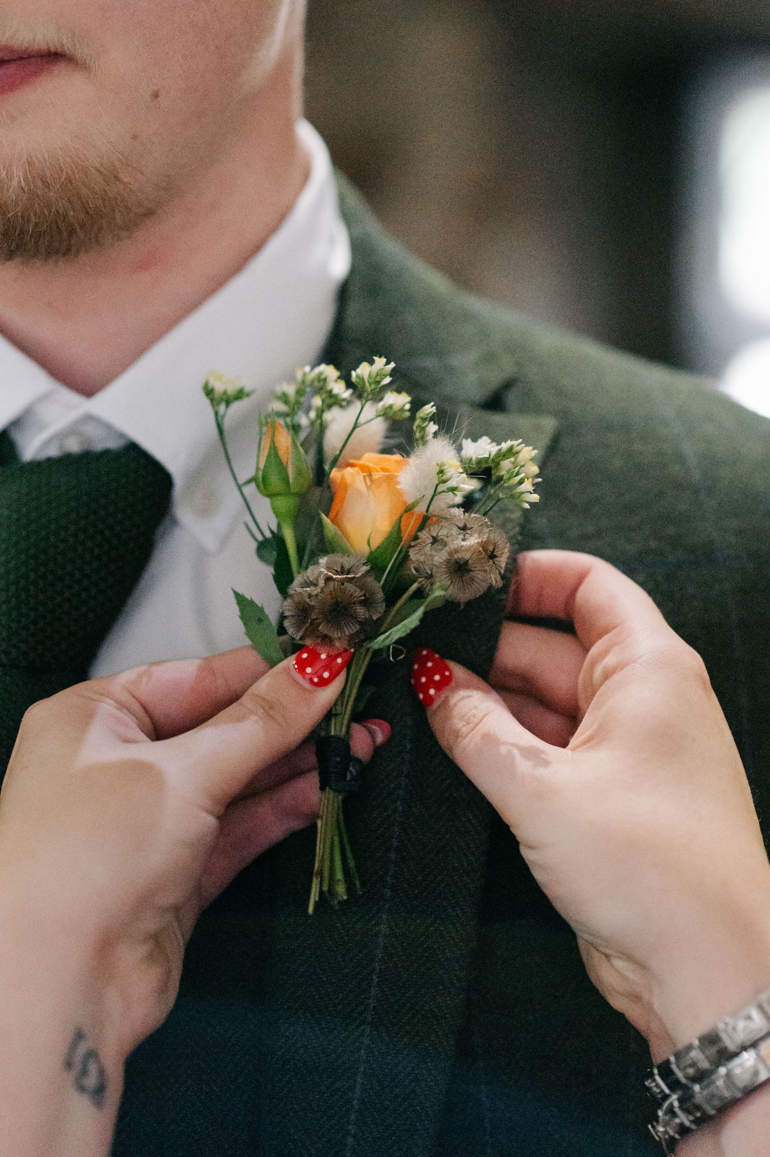 Hands pinning orange and white boutonniere with polka dot ribbon onto dark suit lapel.