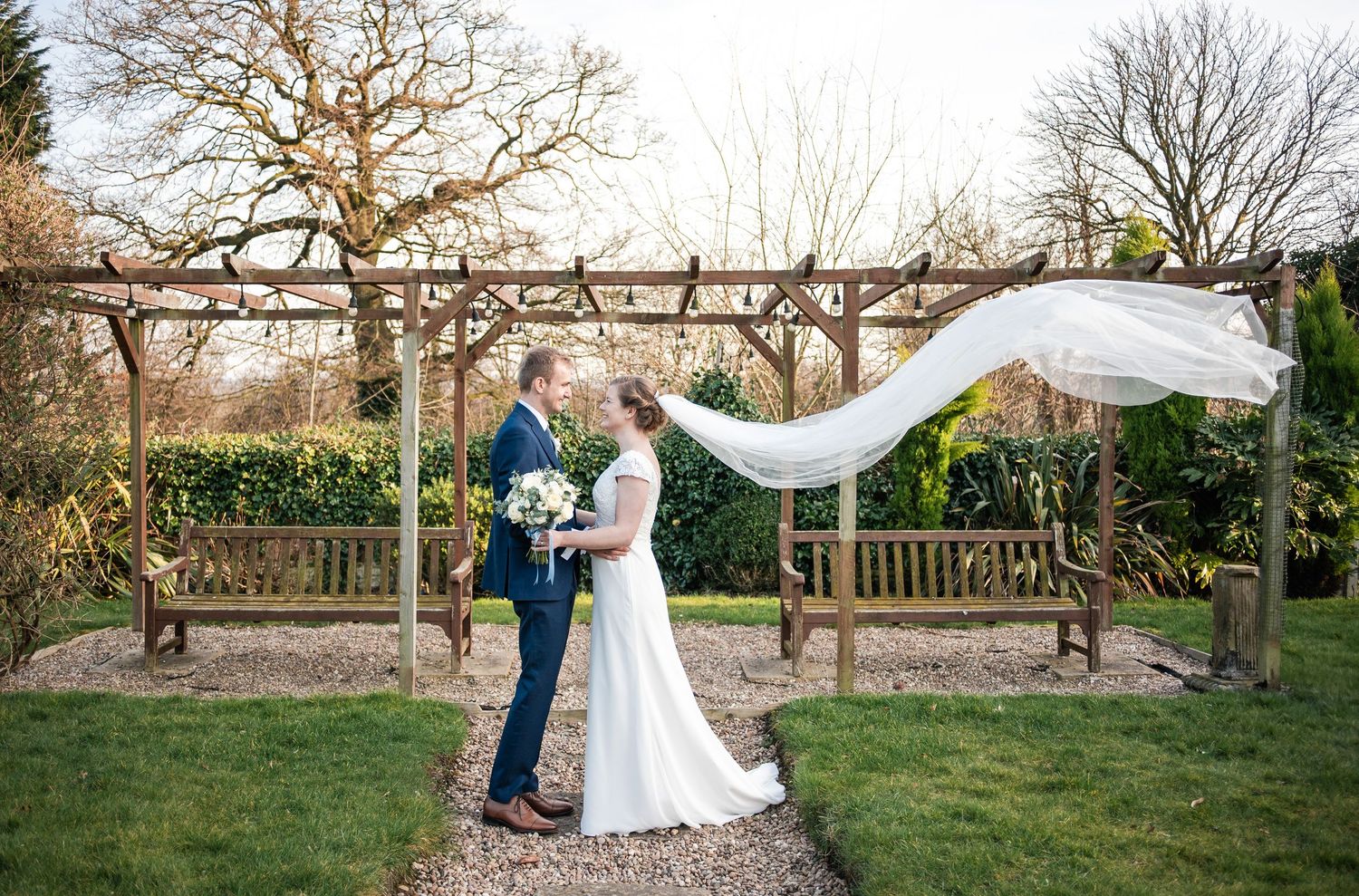 A romantic wedding moment captured in a garden with a flowing veil in the breeze.
