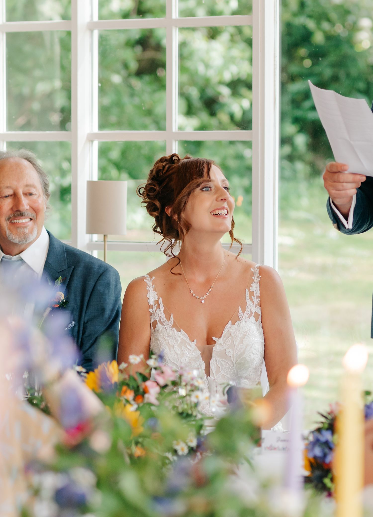 Wedding reception scene in a bright sunroom with floral centerpieces and natural lighting.