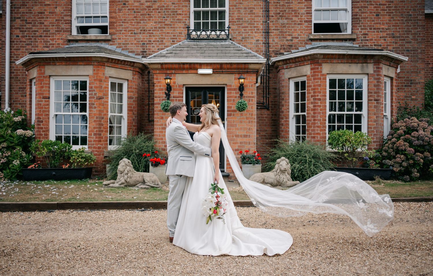 A couple shares a romantic moment outside a historic red brick mansion with a flowing white wedding gown.