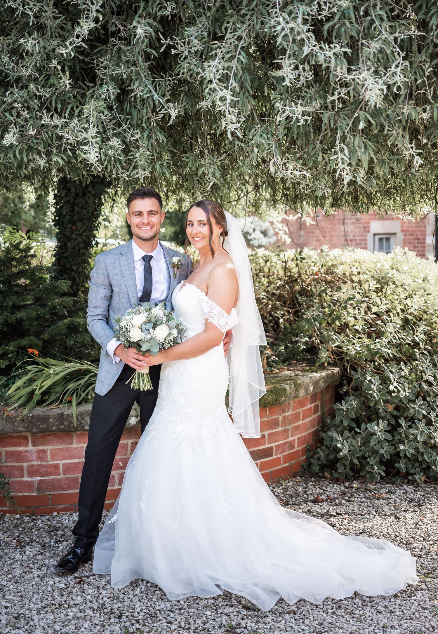 Wedding portraits against brick wall with lush greenery and confetti scattered on ground.