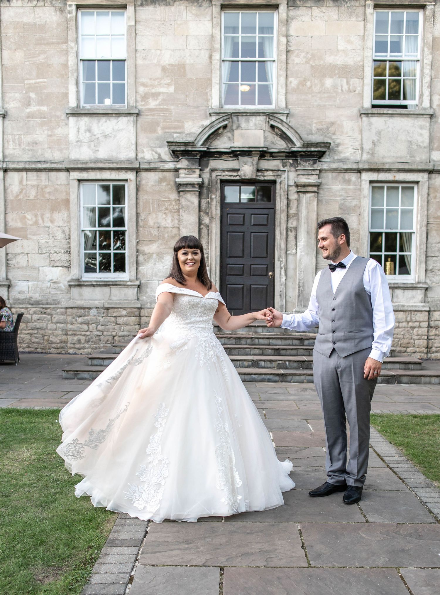 A wedding couple poses outside a historic stone building with elegant Georgian architecture.
