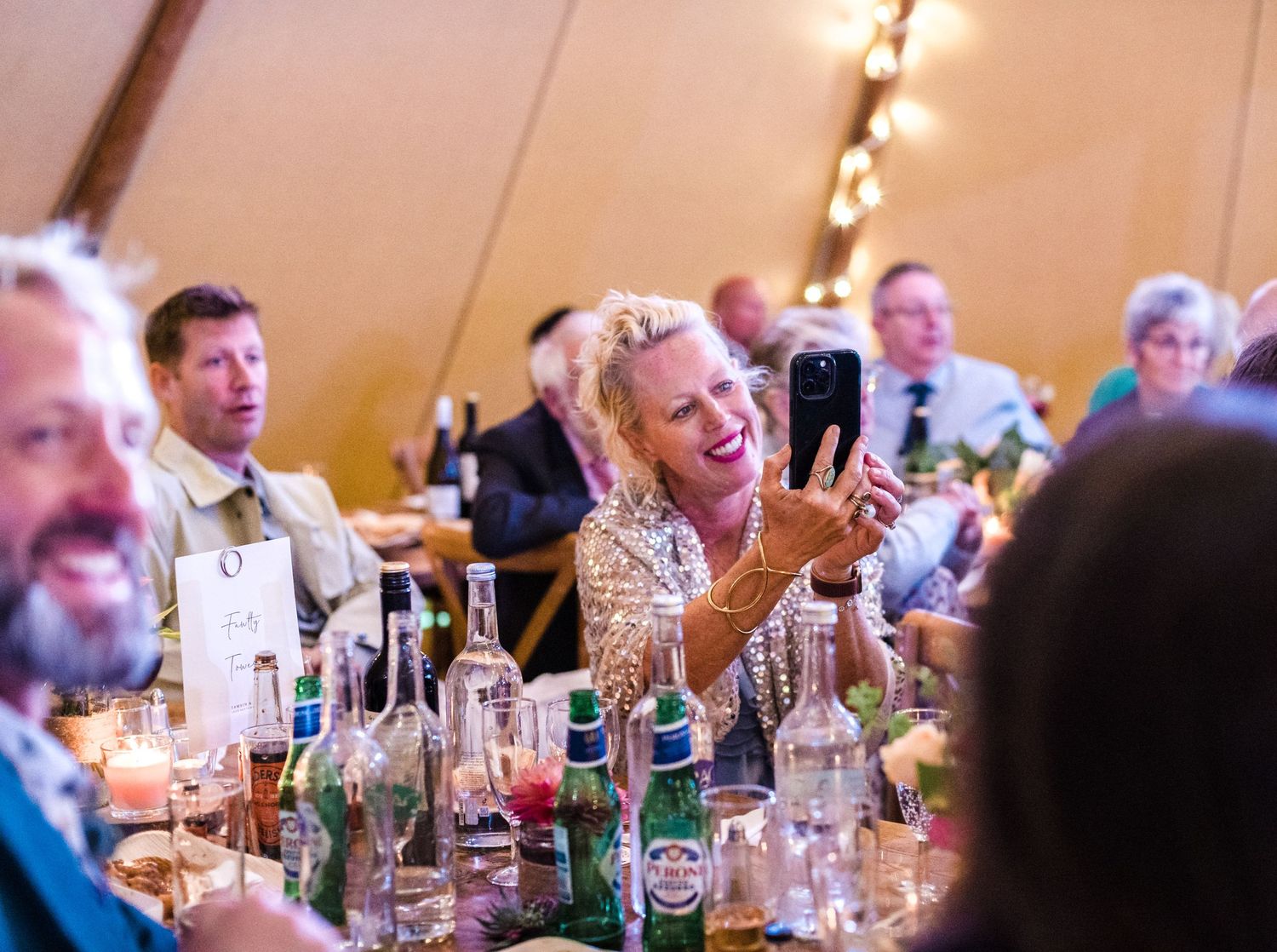 Festive dinner reception inside a tipi tent with string lights and table settings.
