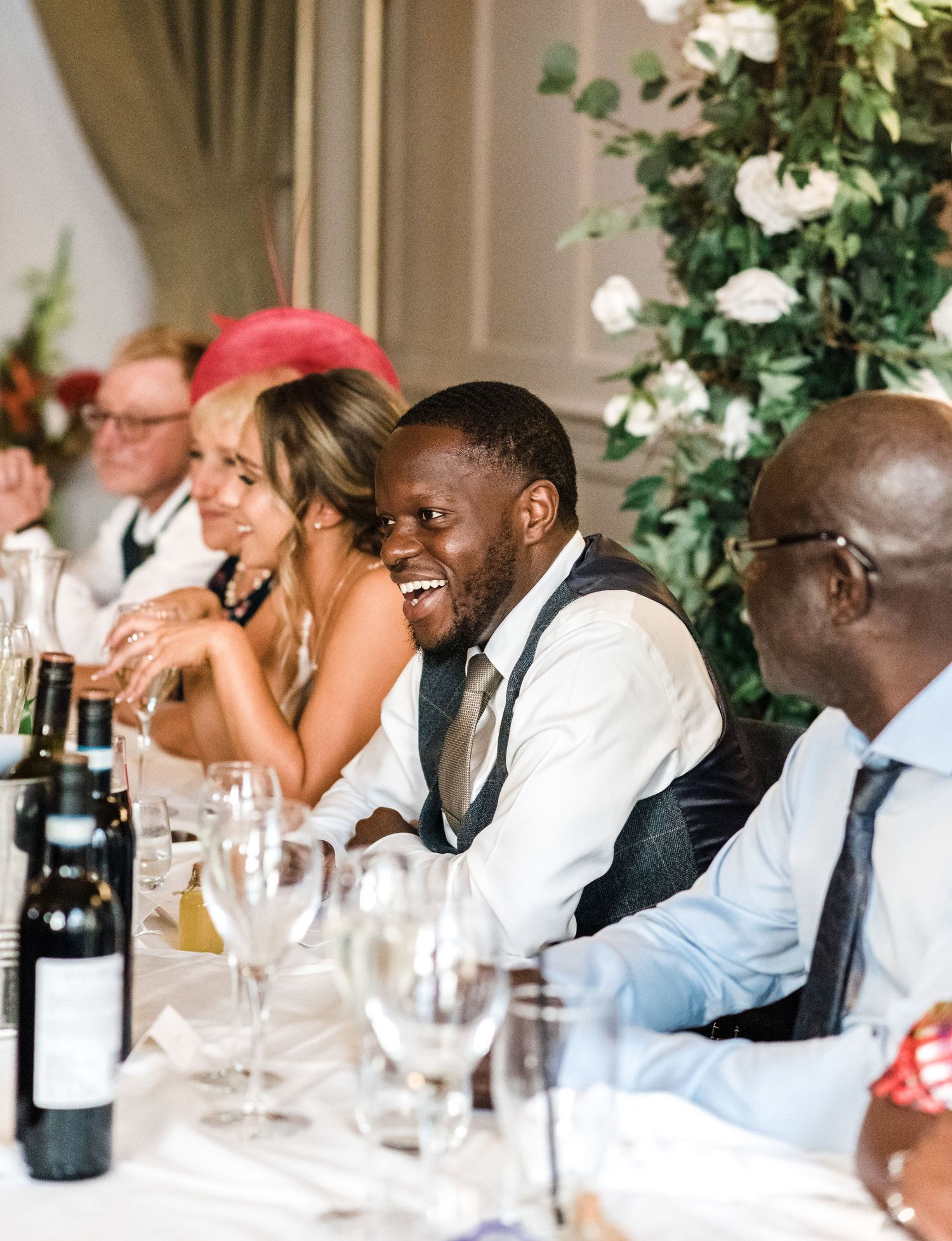 Wedding guests seated at dining table with wine bottles and glasses sharing laughter.