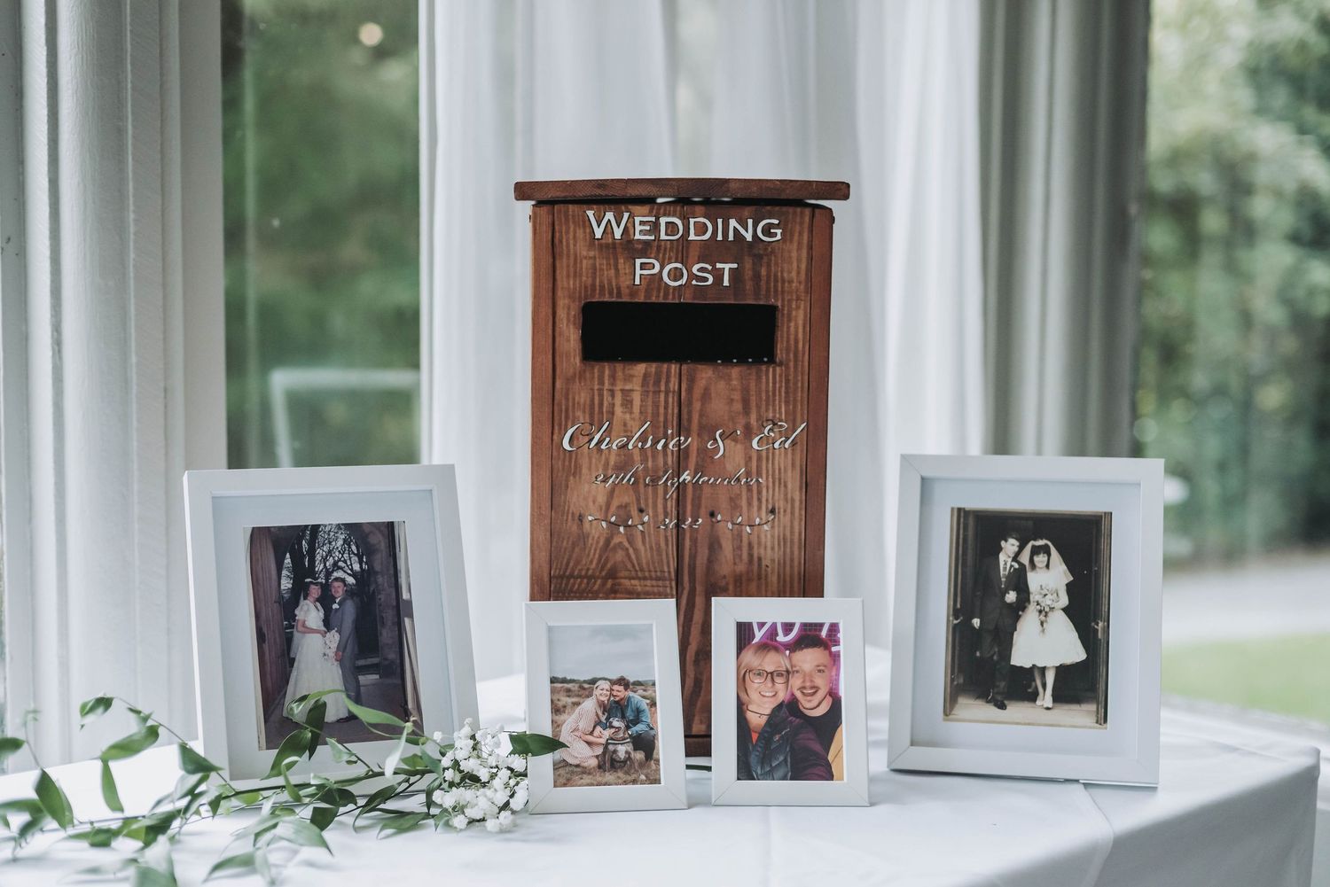 Wedding decor display featuring a wooden post box with framed photographs and greenery.