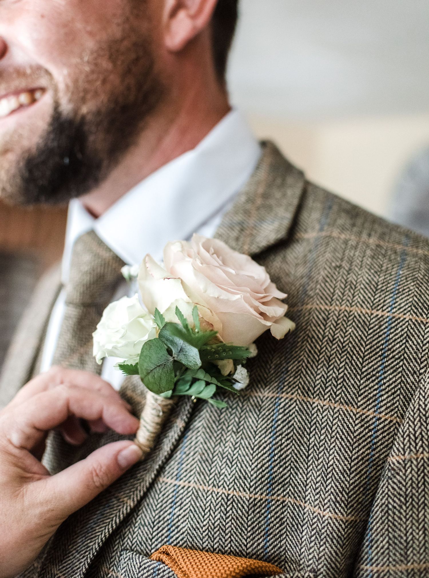 A close-up of a blush pink rose boutonniere pinned to a grey tweed suit jacket.