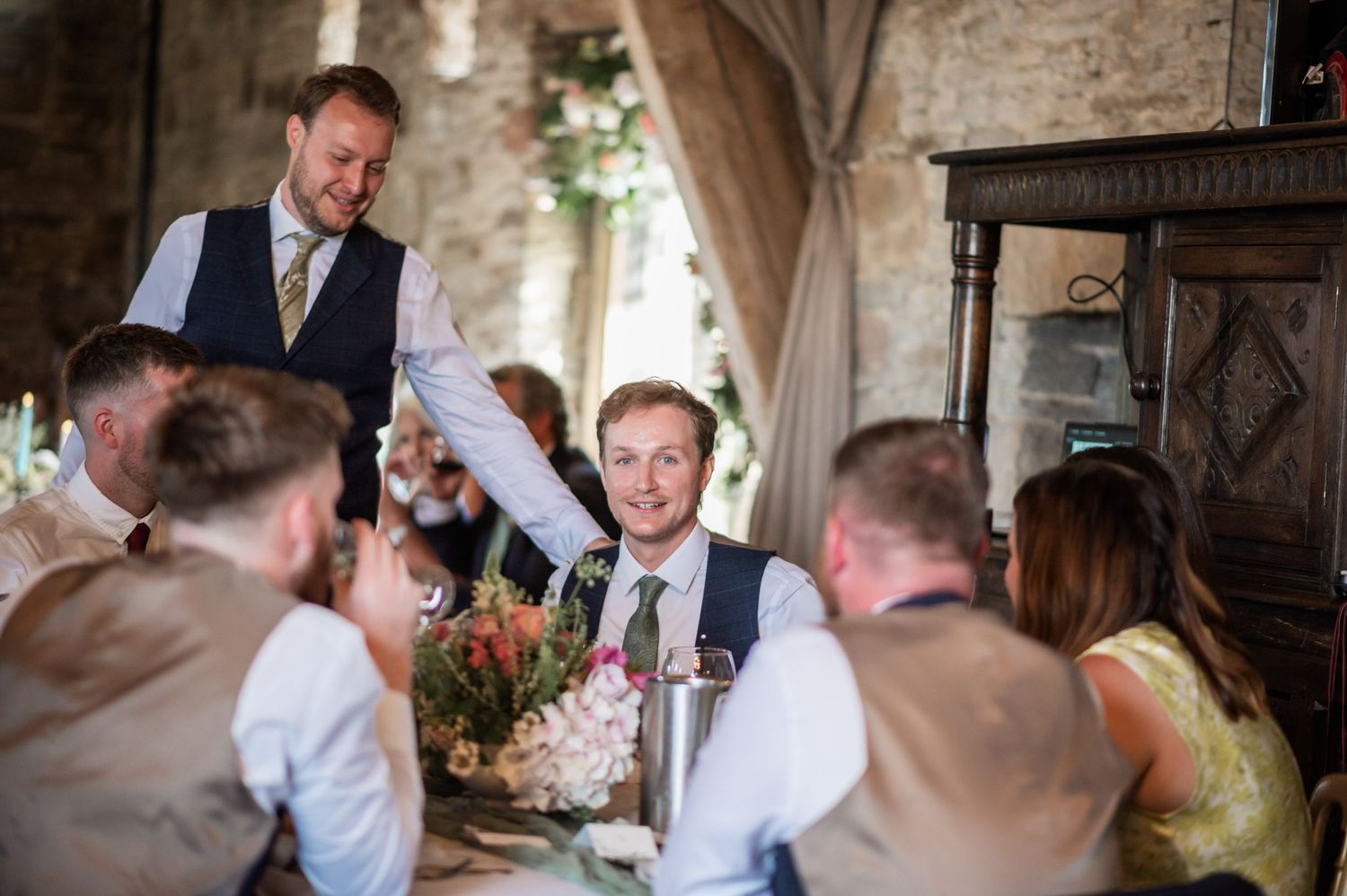 Wedding guests toasting during speeches at a rustic venue reception.