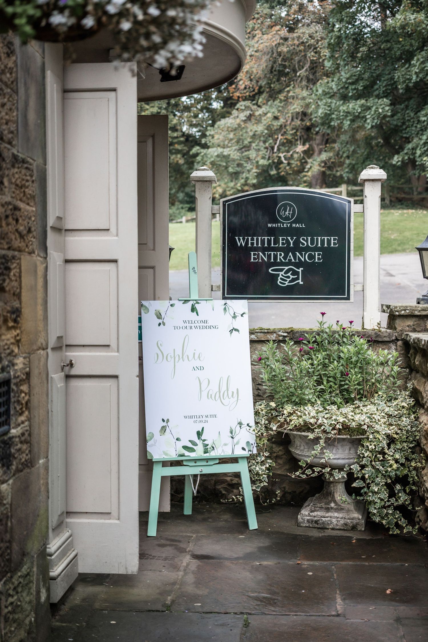 Whitley Suite entrance sign and welcome board displayed on a mint green easel outside stone building.