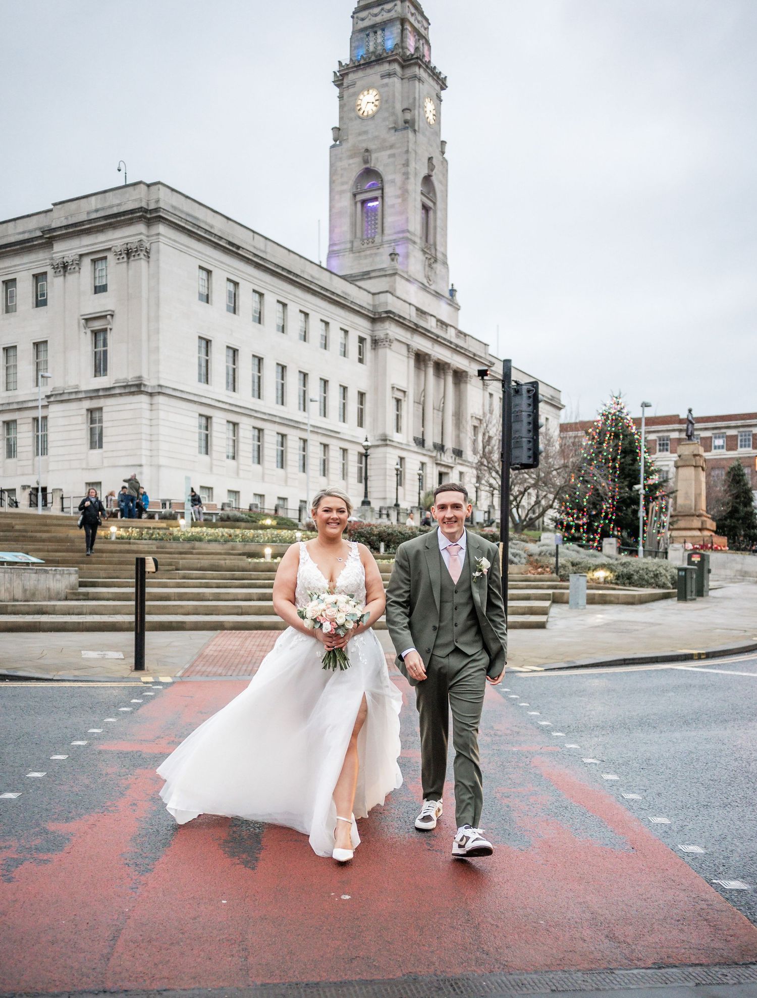 Wedding couple poses in front of a historic clock tower and government building on a red-painted street.