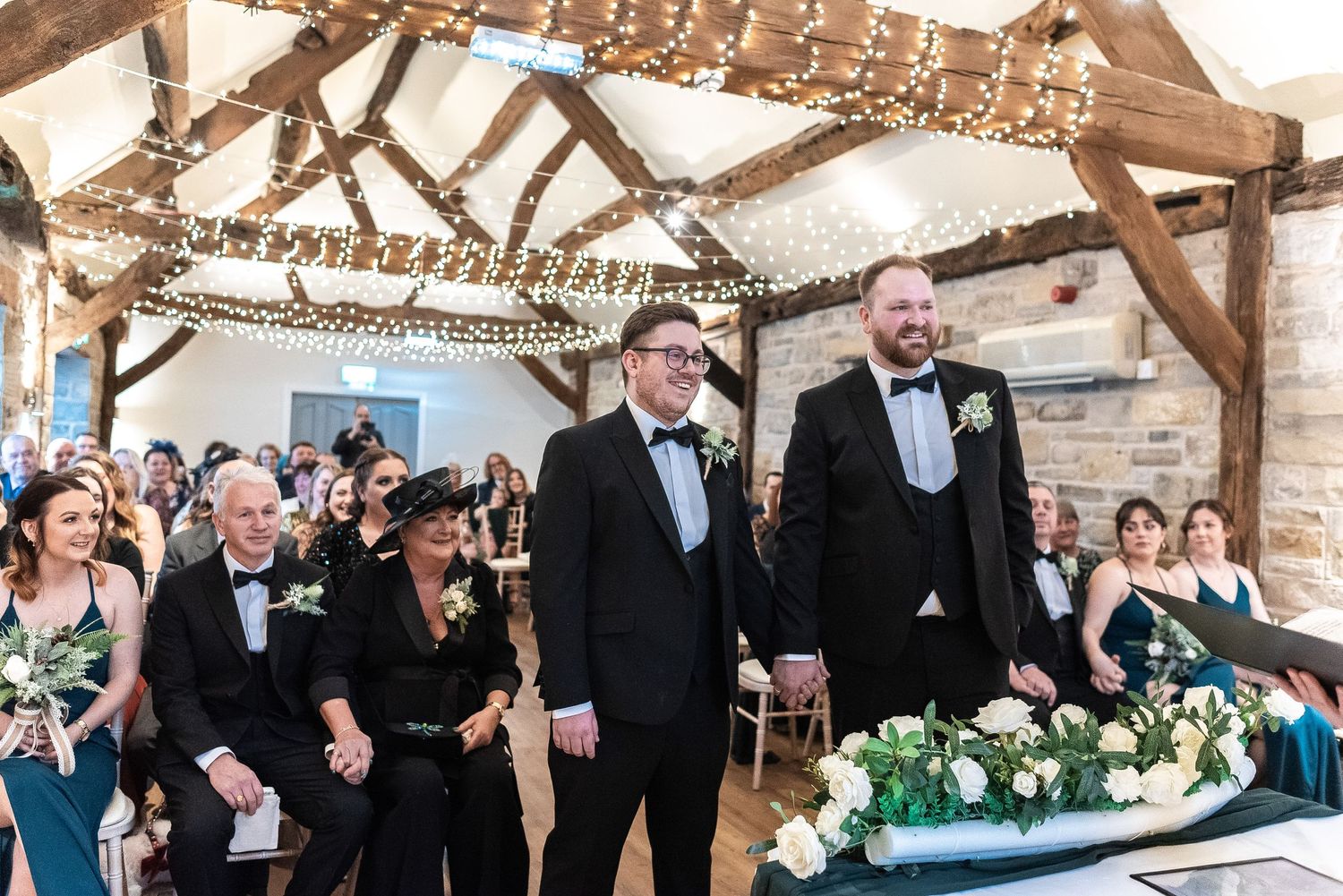 Wedding ceremony in rustic barn venue with exposed wooden beams and twinkle lights.