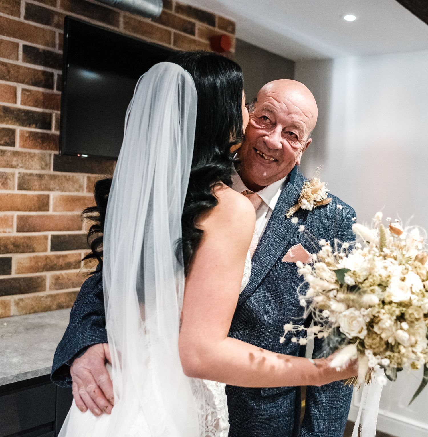 An emotional embrace shared during wedding celebrations against exposed brick wall.