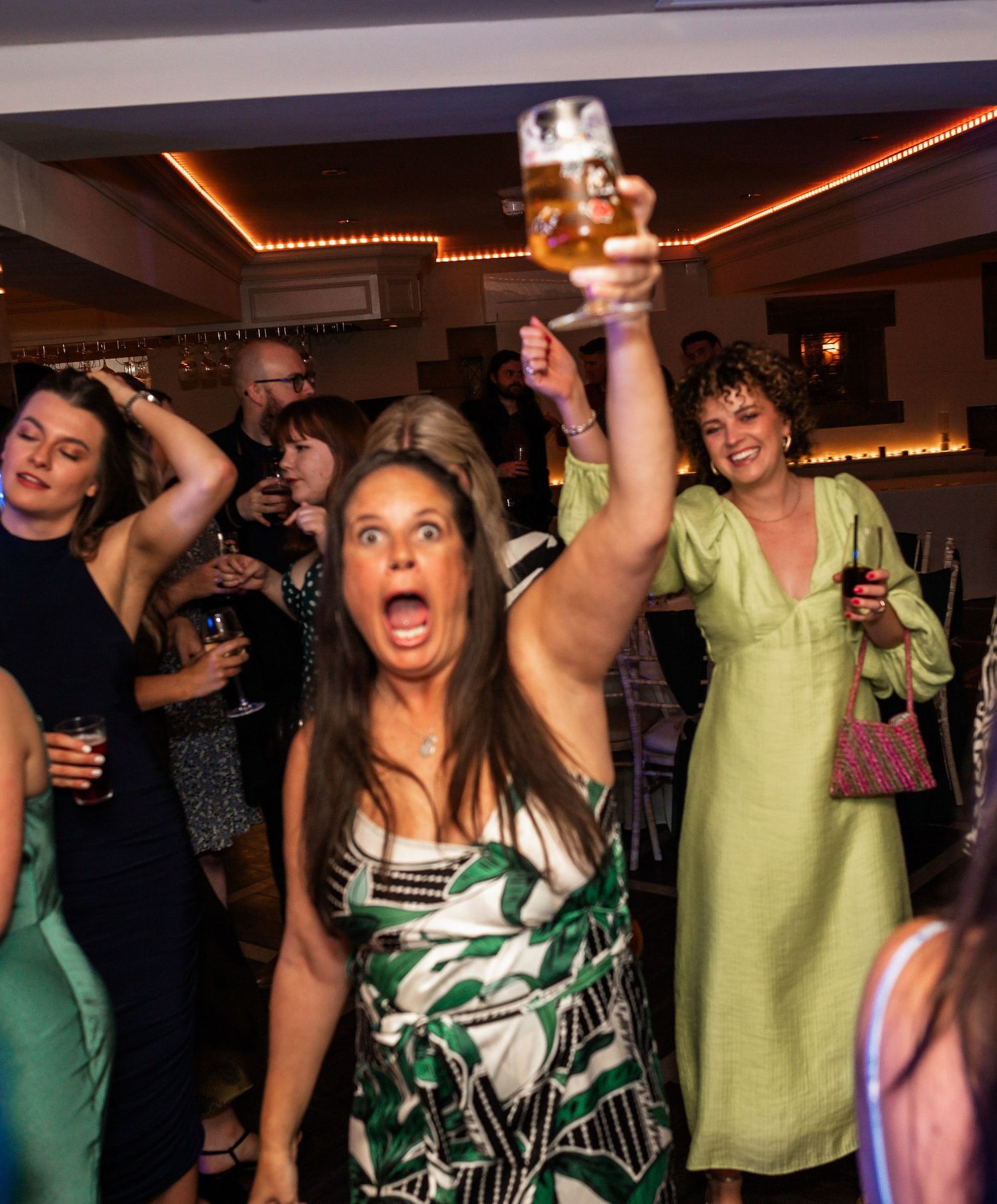 Party guests dancing enthusiastically at wedding reception with colorful mood lighting.