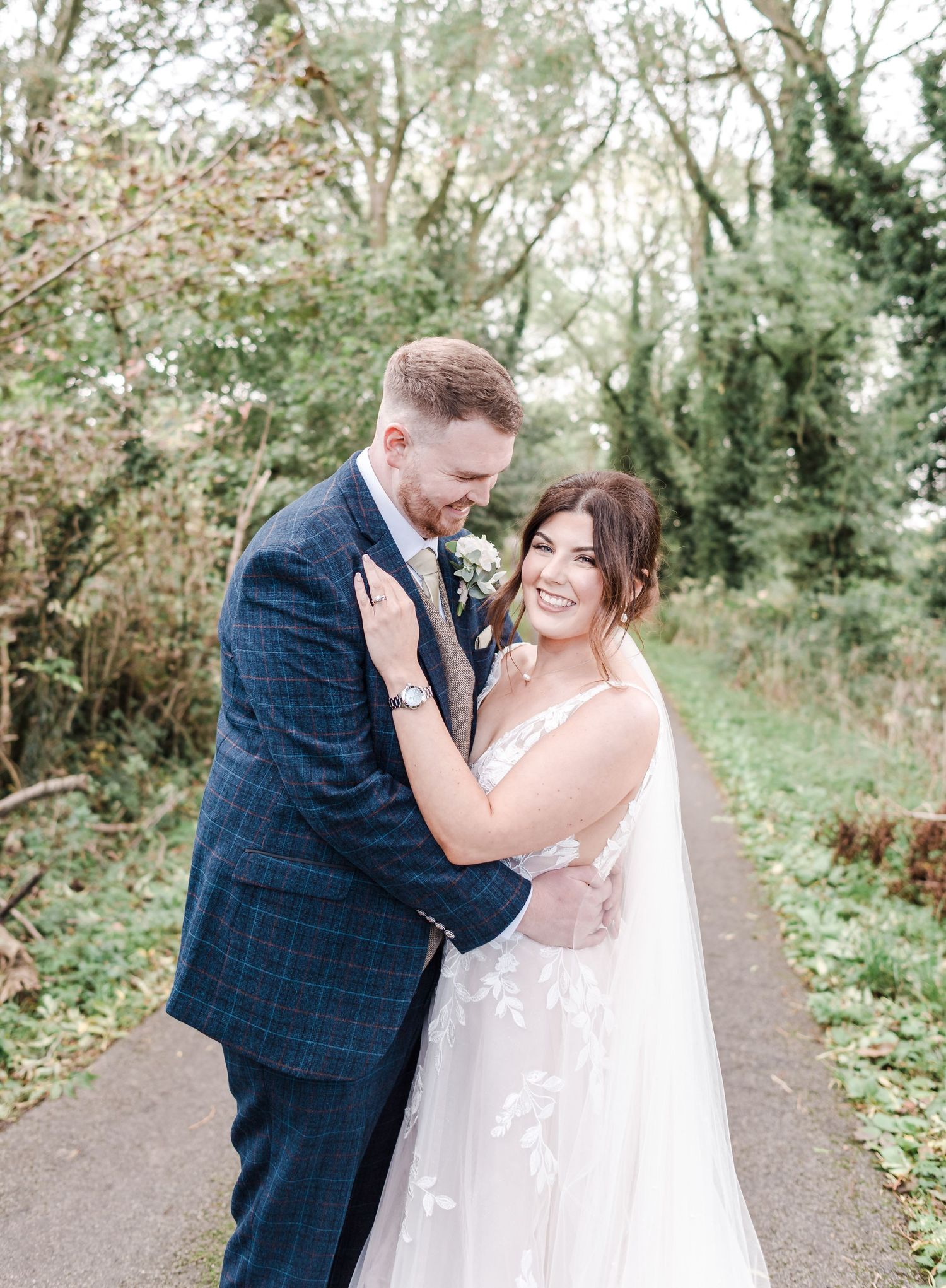 Happy couple embraces on a woodland path during their wedding photoshoot.