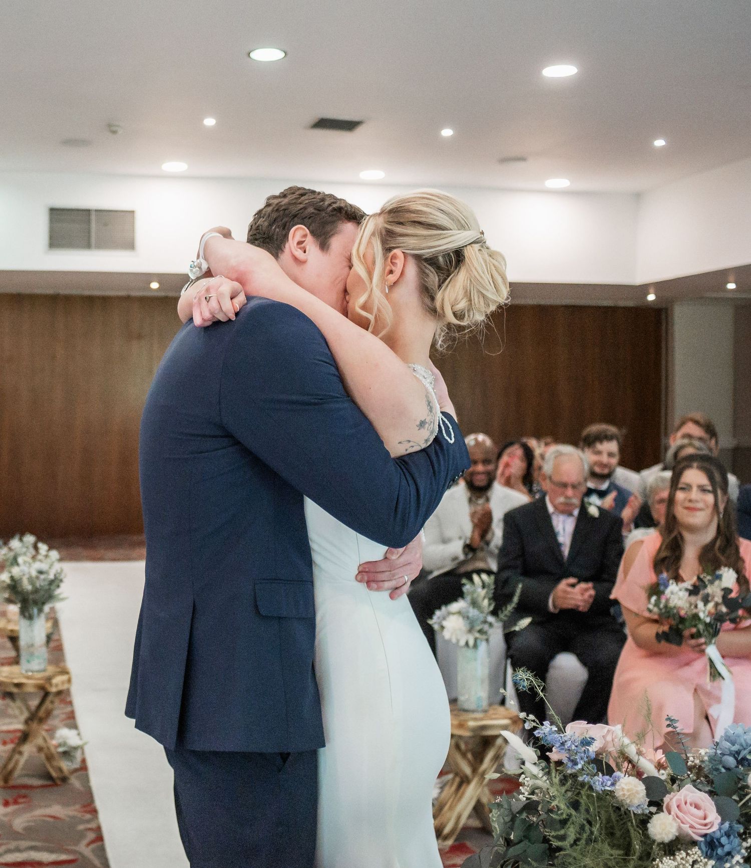 Newlyweds share their first kiss at the altar adorned with pink and white flowers.
