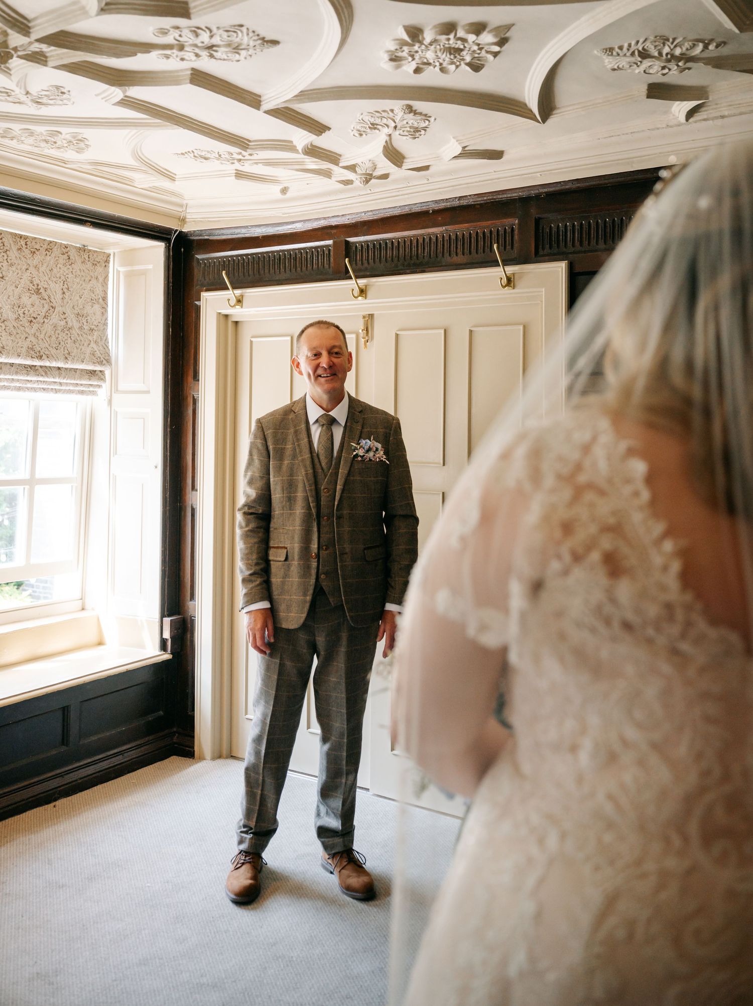 A smiling father in a tweed suit sees his bride daughter for the first time on her wedding day.