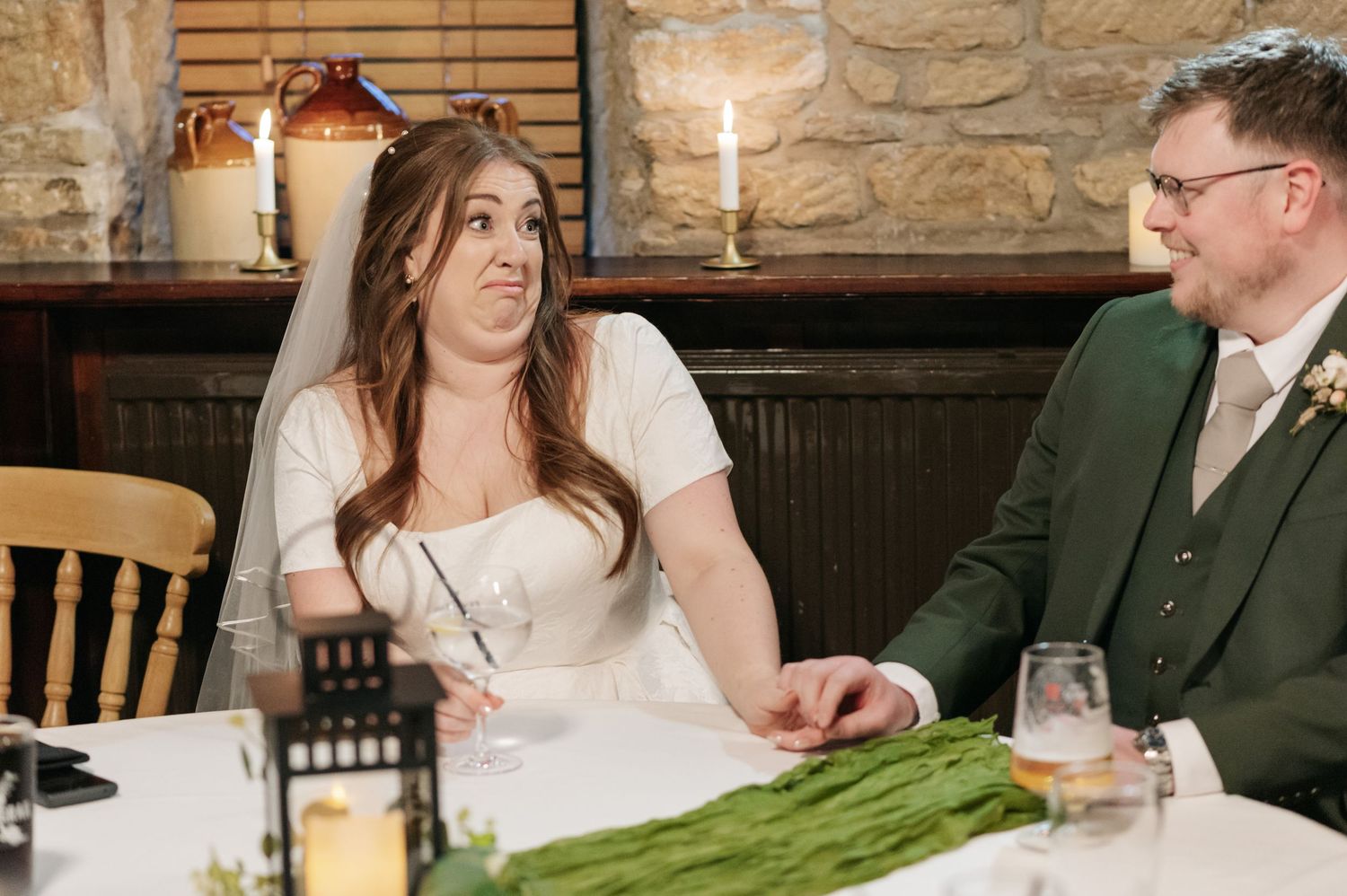 A couple at their wedding reception table with candlelight and rustic stone wall decor.