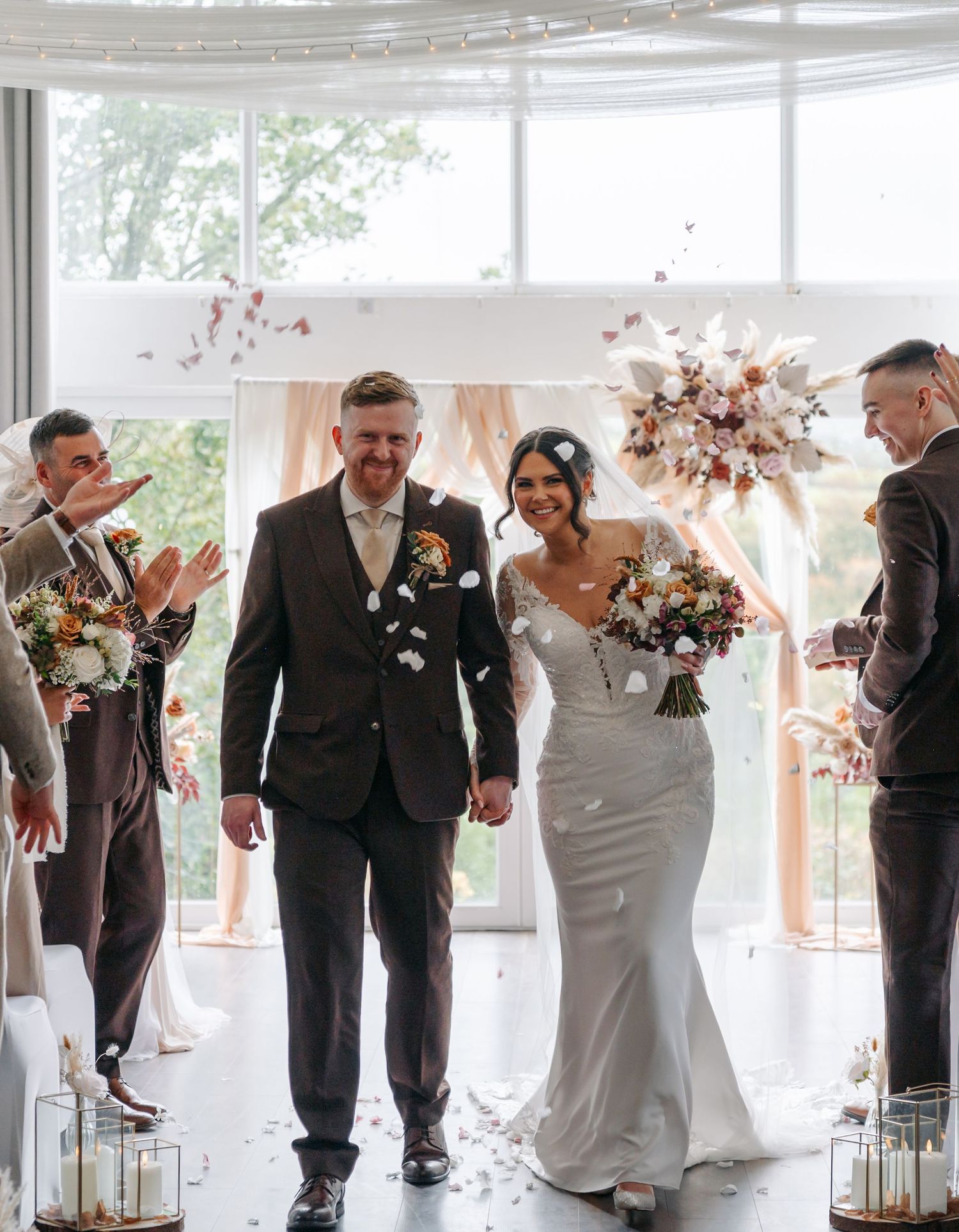 A wedding party lineup in a bright room with large windows and floral decorations.