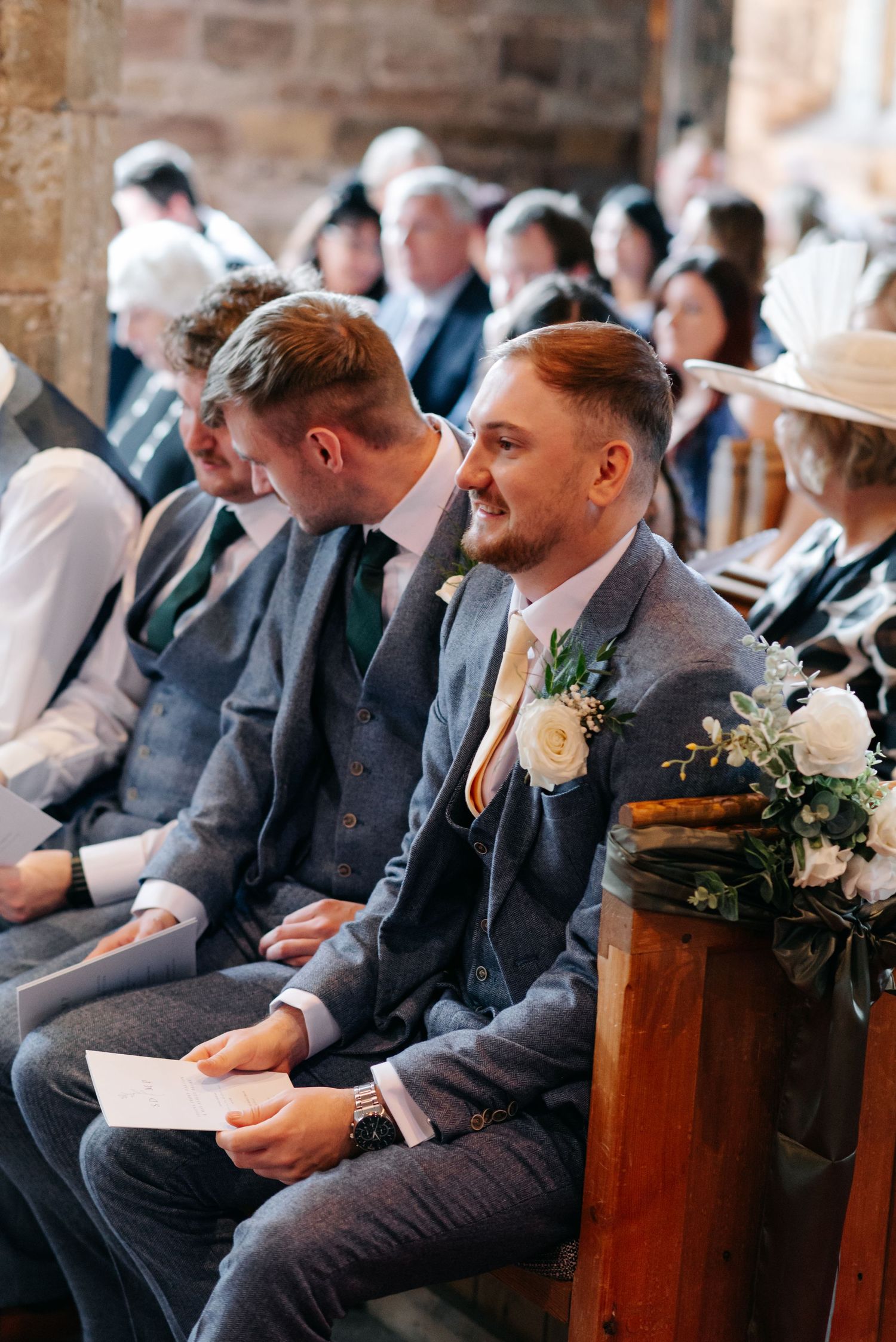 Wedding guests seated in rows at a rustic brick venue with floral decorations.