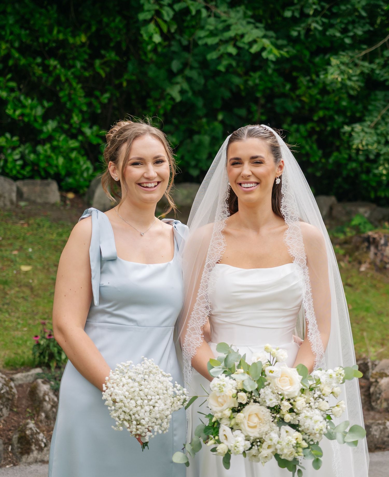 Bridesmaids in light blue dresses and bride in white hold bouquets of white flowers in garden setting.