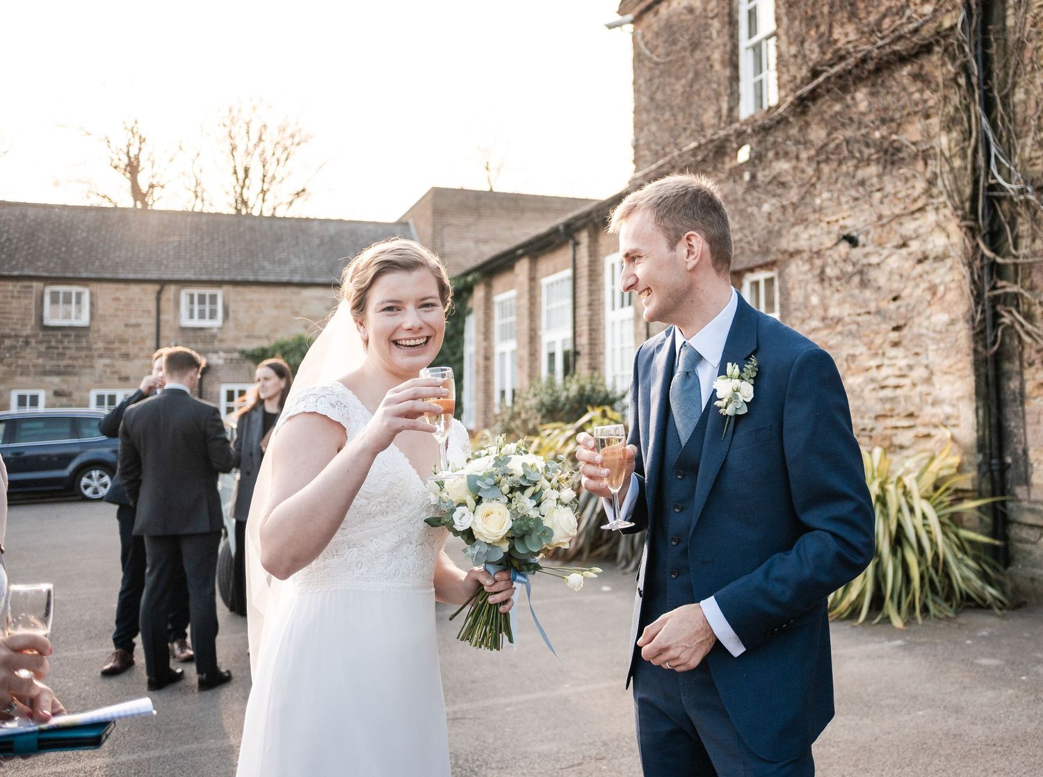 Wedding couple shares joyful moments in front of rustic stone wall during outdoor celebration.