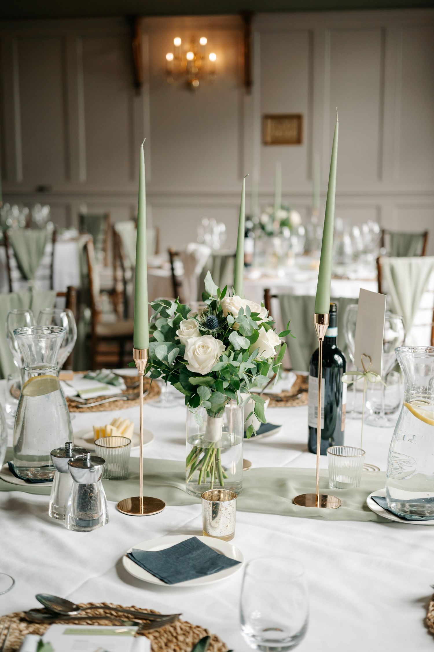 Elegant wedding reception table setting with white linens, tall green candles, and delicate floral centerpieces.