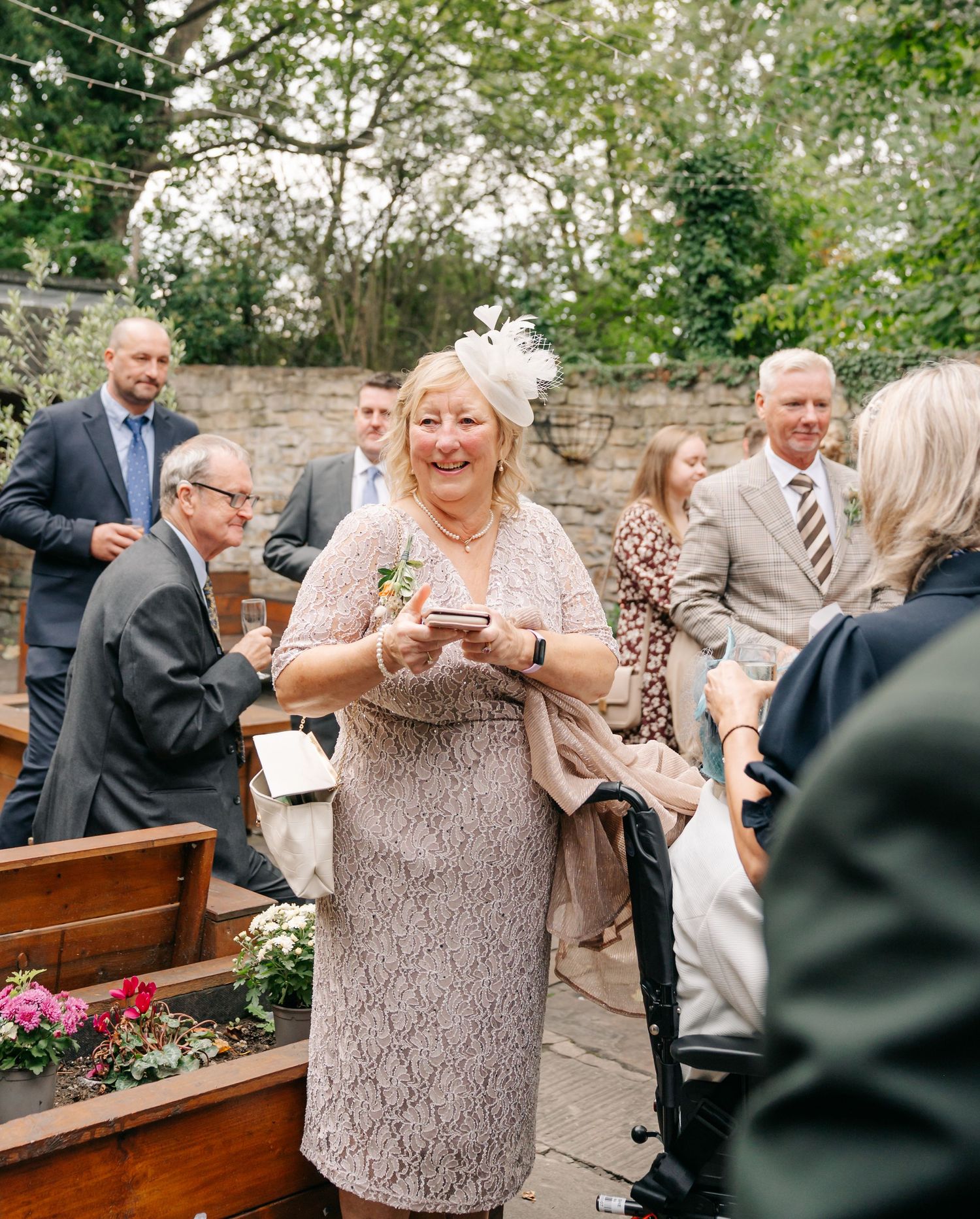 Wedding guests mingle and celebrate at an outdoor reception with wooden benches.