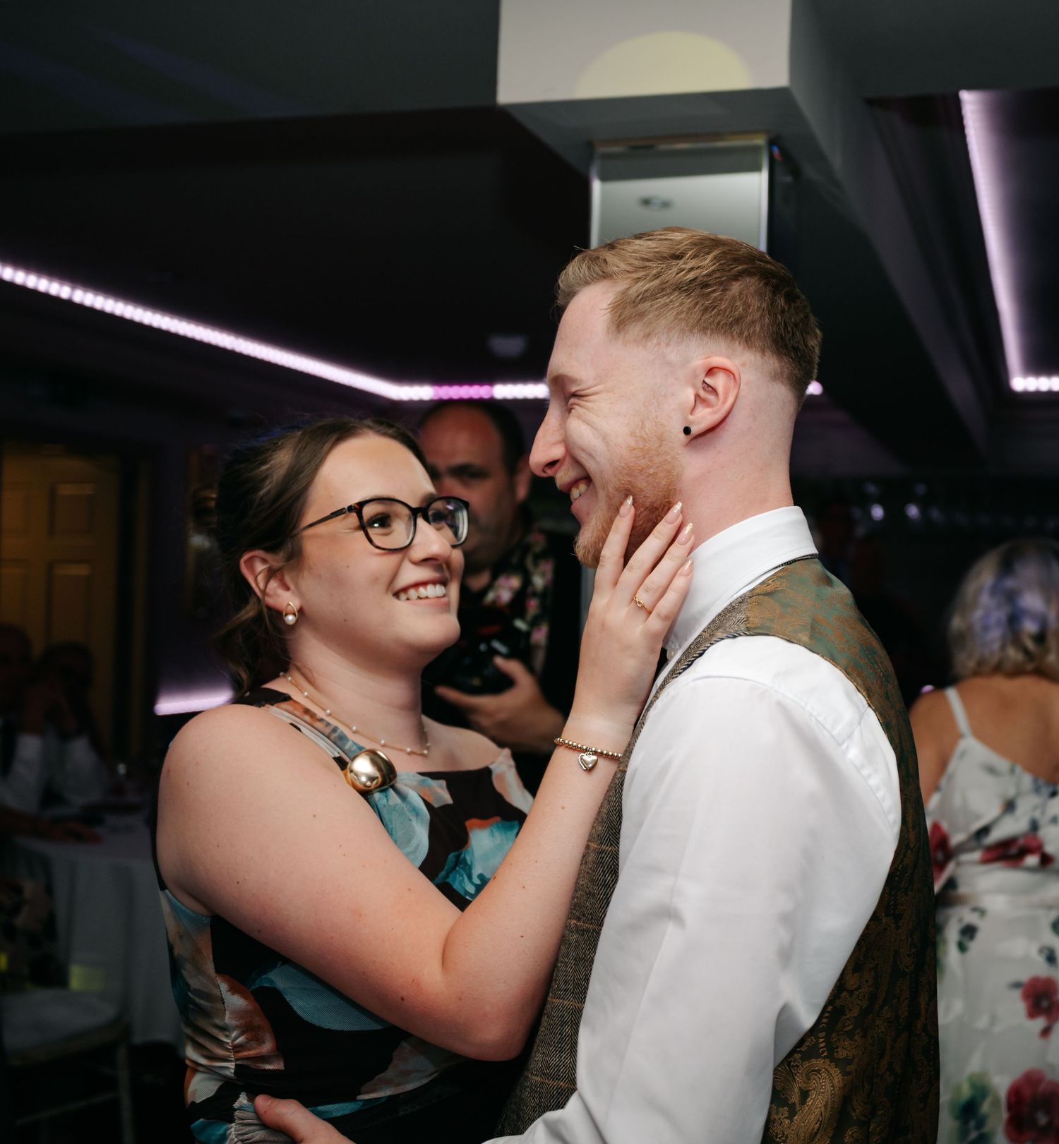 Couple sharing a tender moment on the dance floor at an indoor wedding reception with purple lighting.