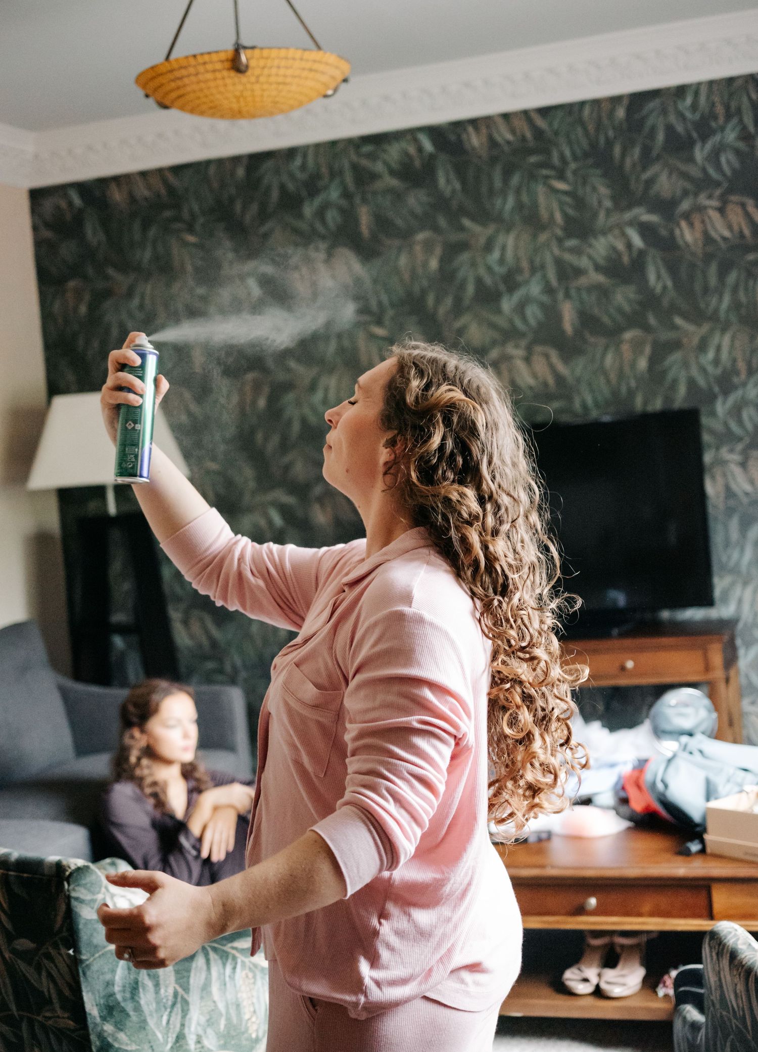 Someone in a pink blazer dances joyfully in a room with dark floral wallpaper.