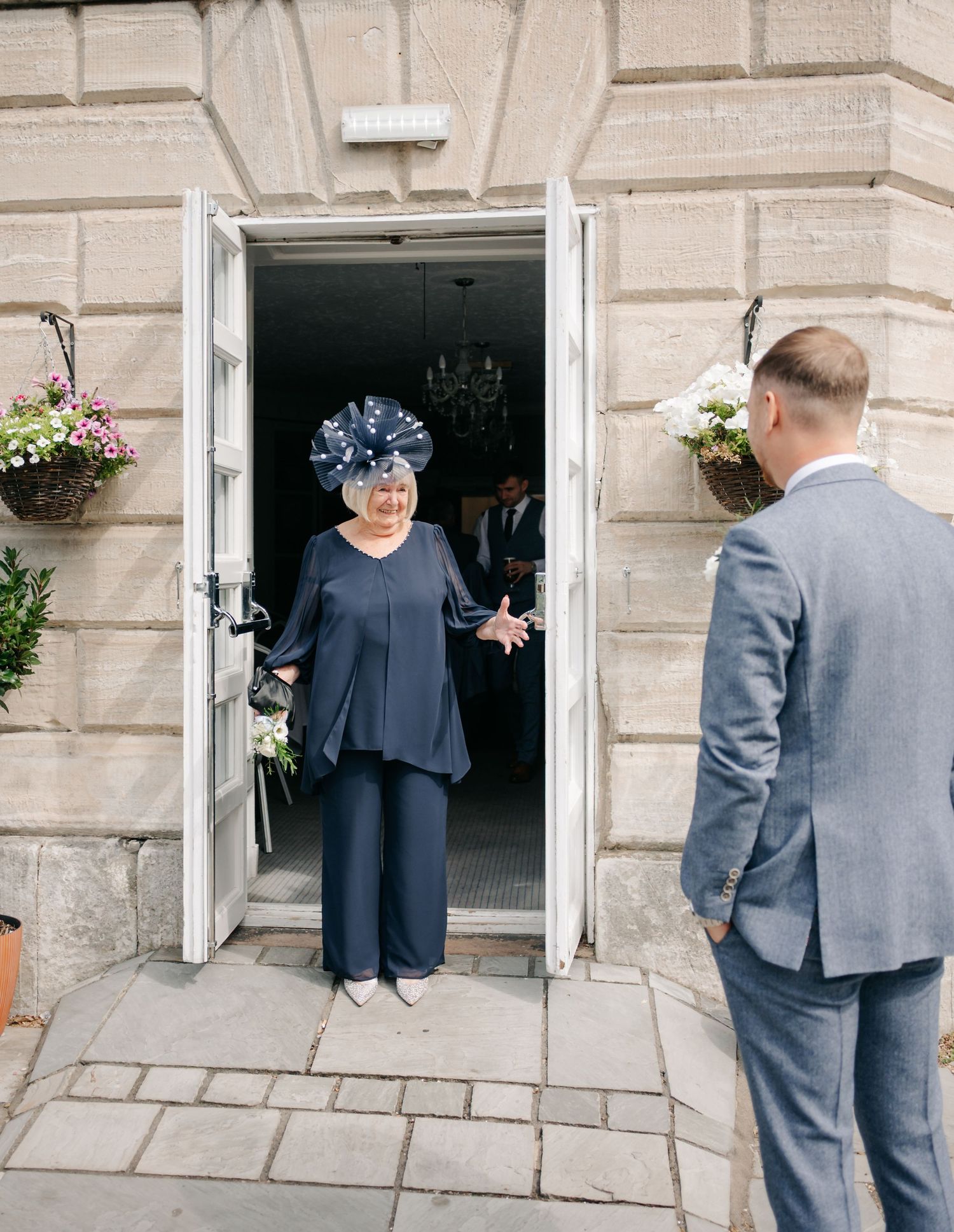 Two people conversing at an elegant doorway adorned with hanging flower baskets at a formal event.