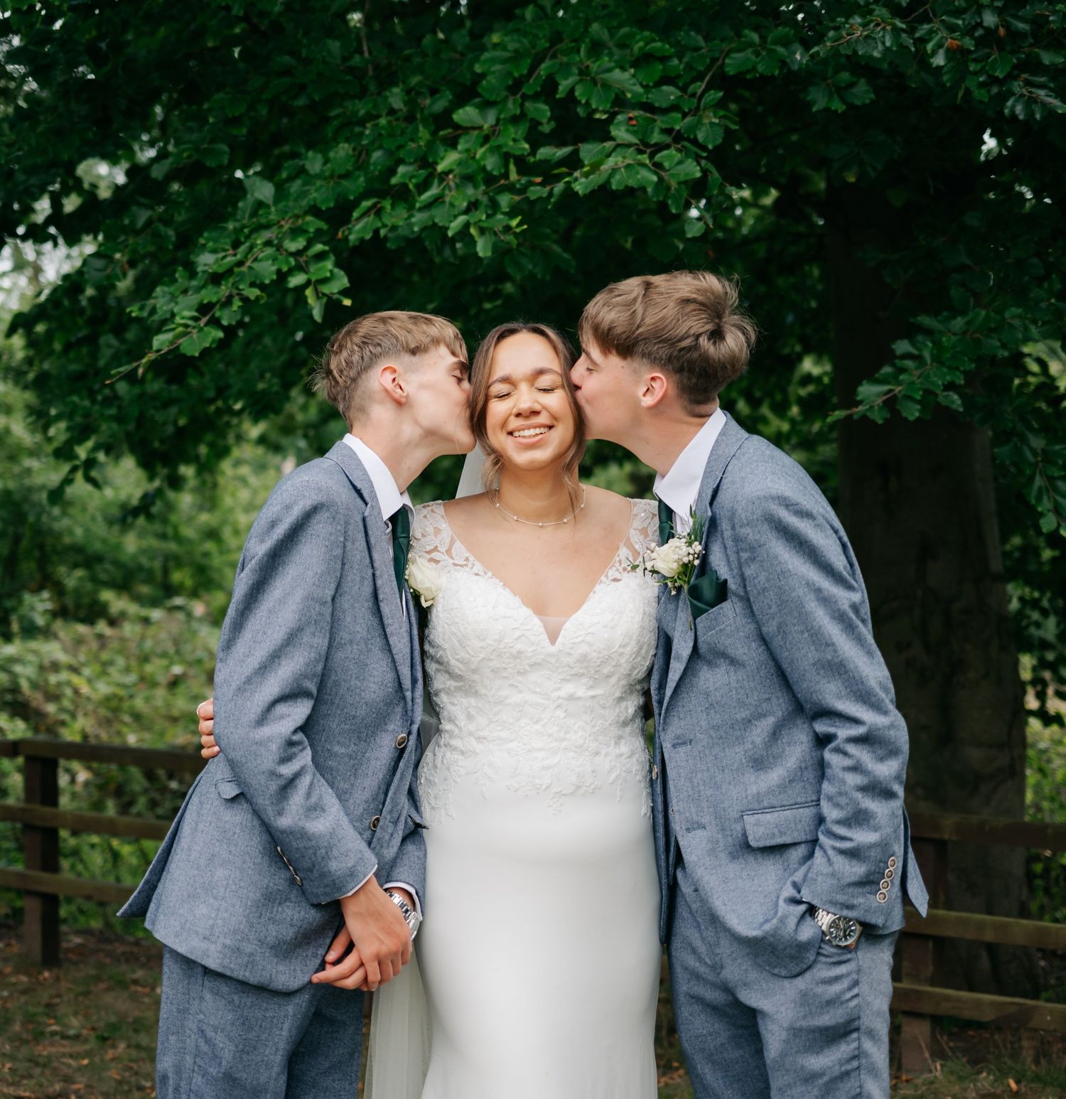 Wedding party in gray suits and white dress posing together outdoors.