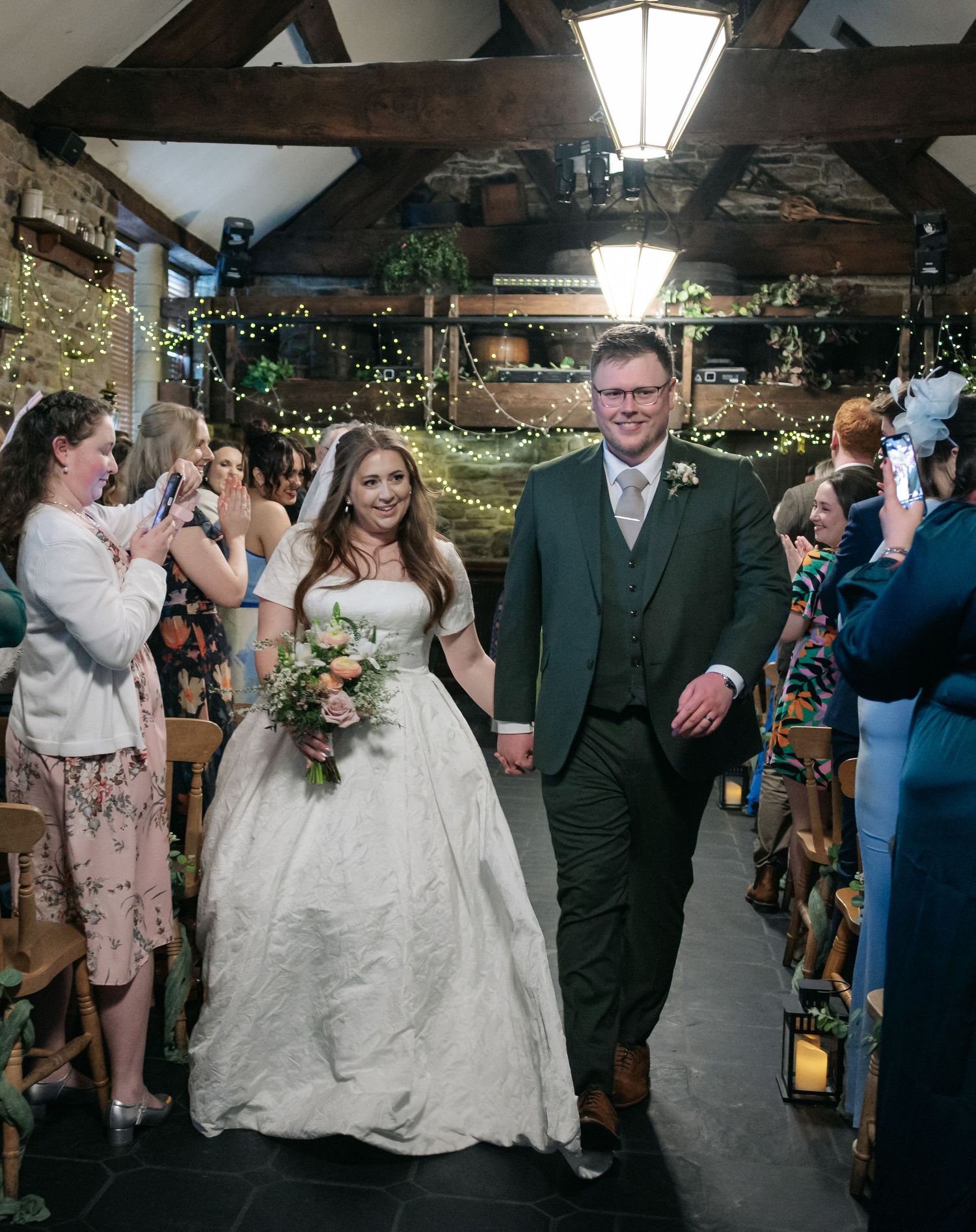 Wedding couple walking down the aisle while guests capture photos of the joyous moment.