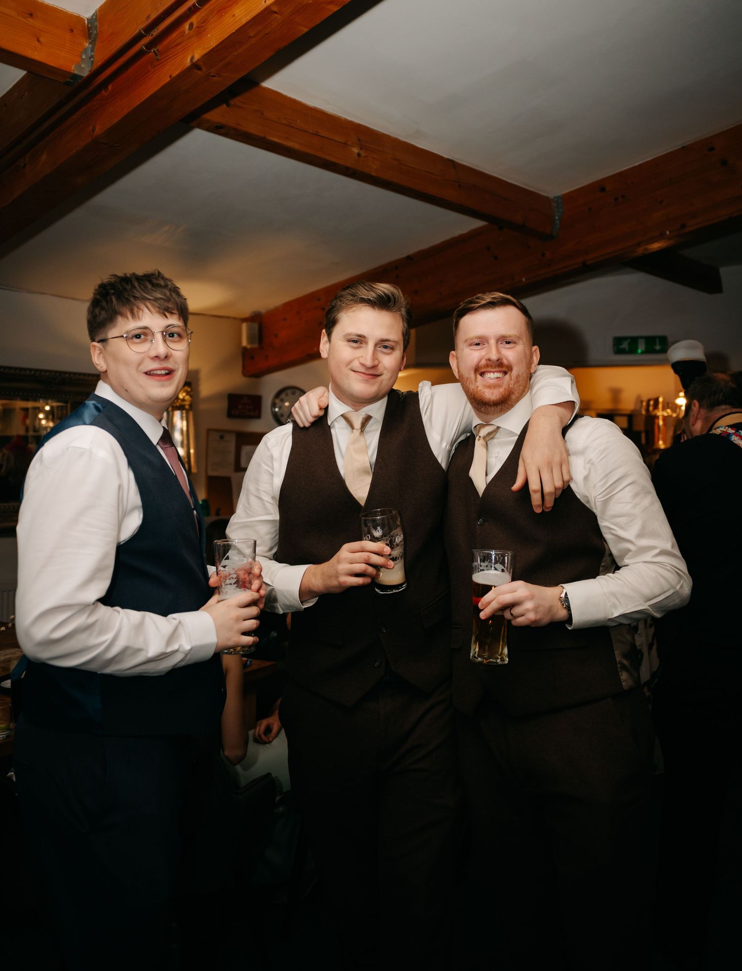 Groomsmen in waistcoats sharing drinks and laughs during wedding reception celebrations.