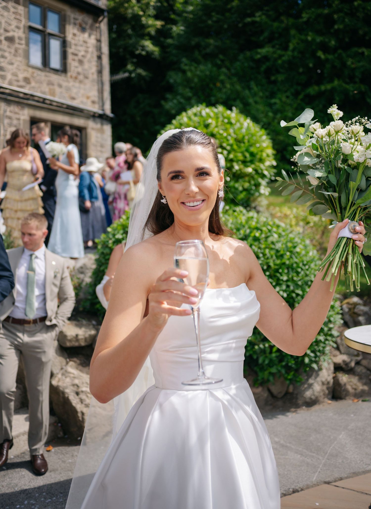 Person in white dress holding champagne glasses during outdoor wedding celebration.