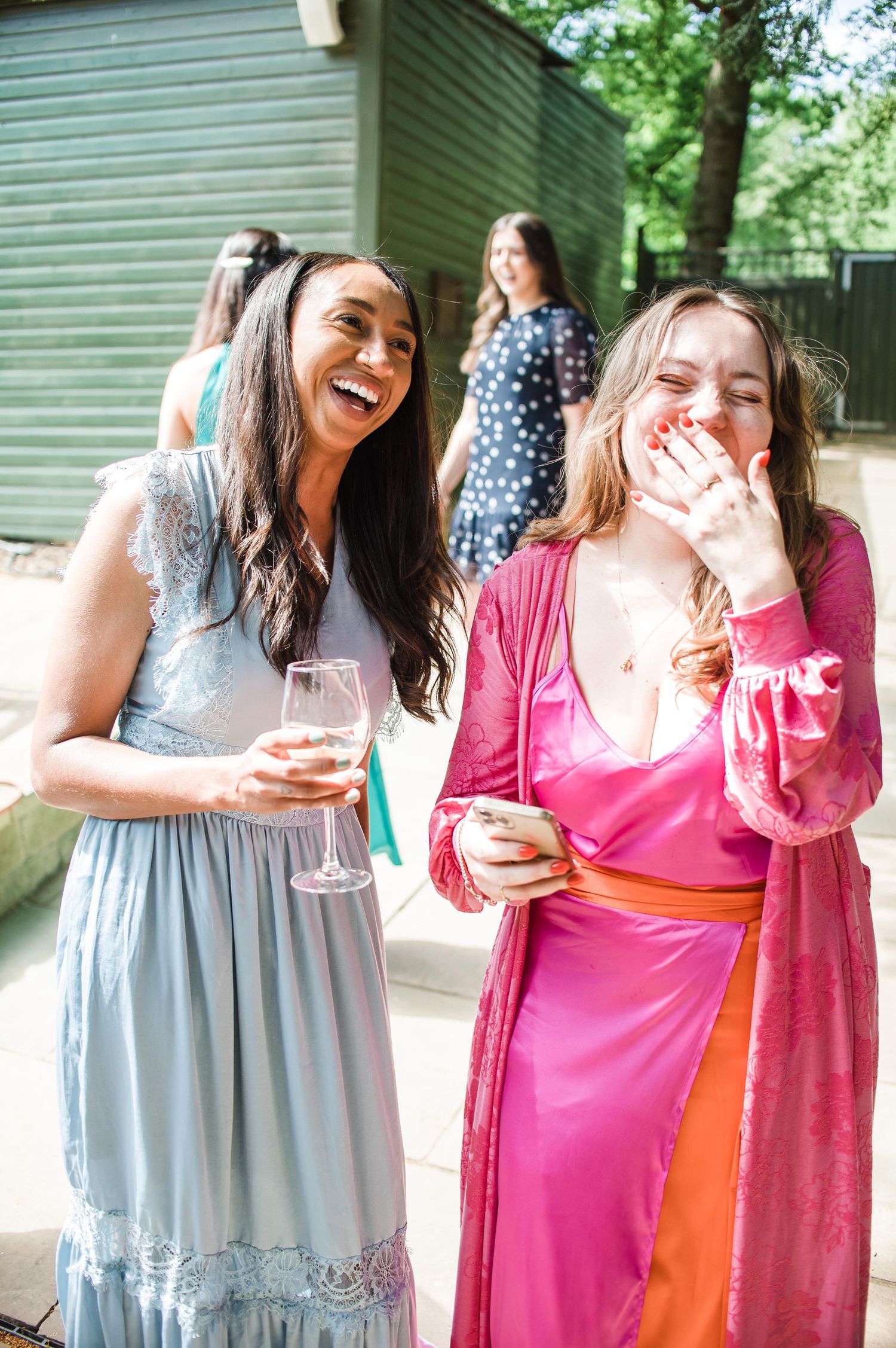 Wedding guests laughing while holding champagne glasses at outdoor reception.
