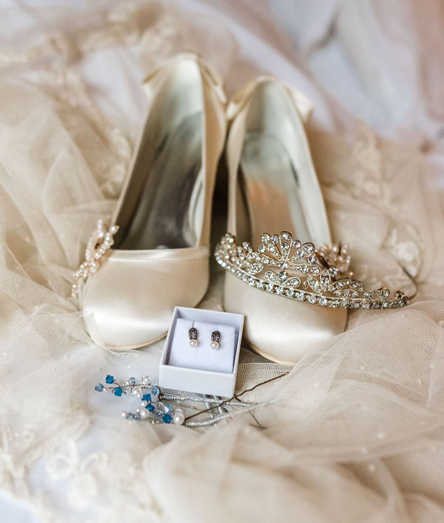 Wedding accessories including white heels, tiara and blue jewelry on lace fabric.