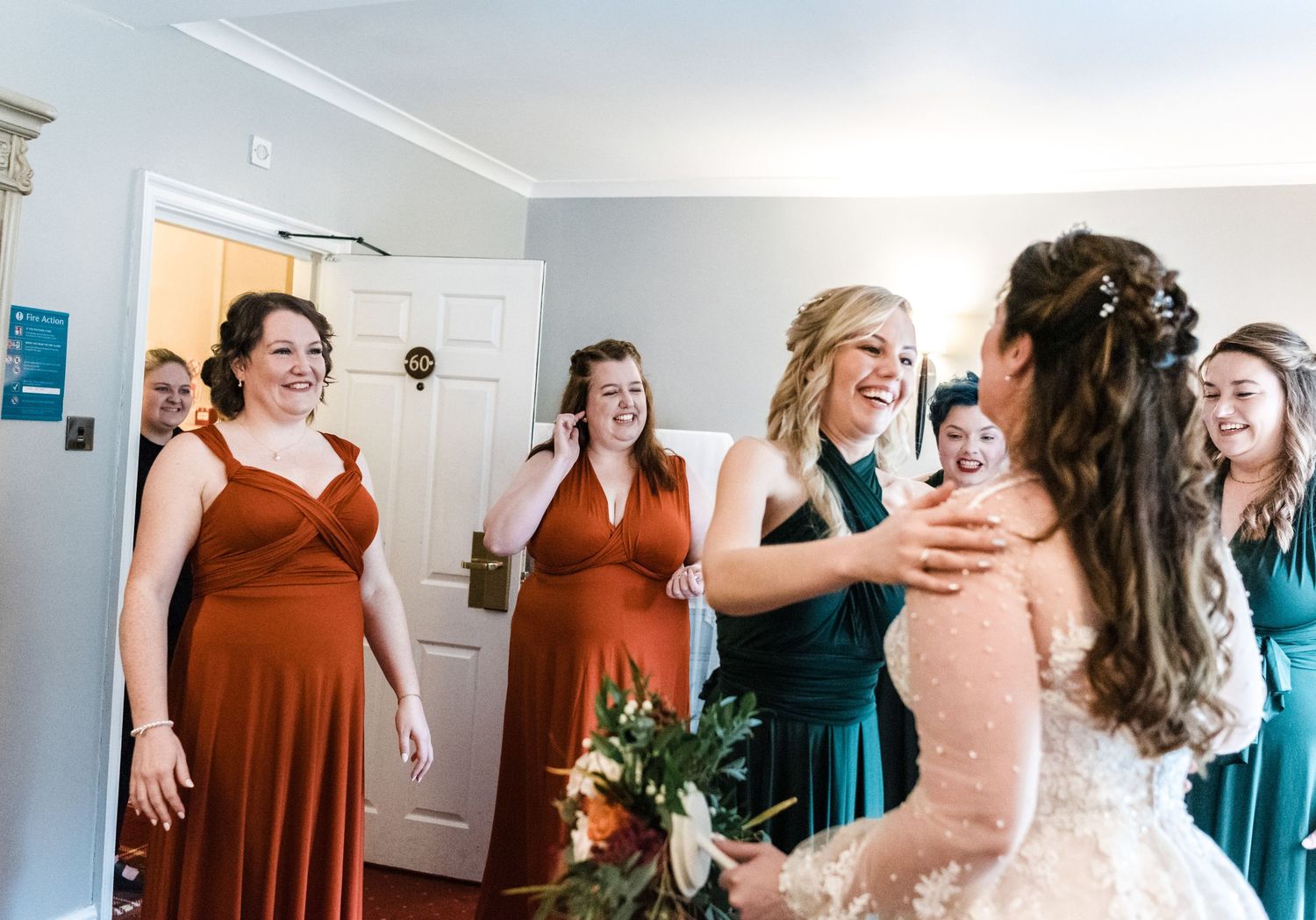 Joyful reaction of bridesmaids in burgundy and green dresses seeing bride for first time.
