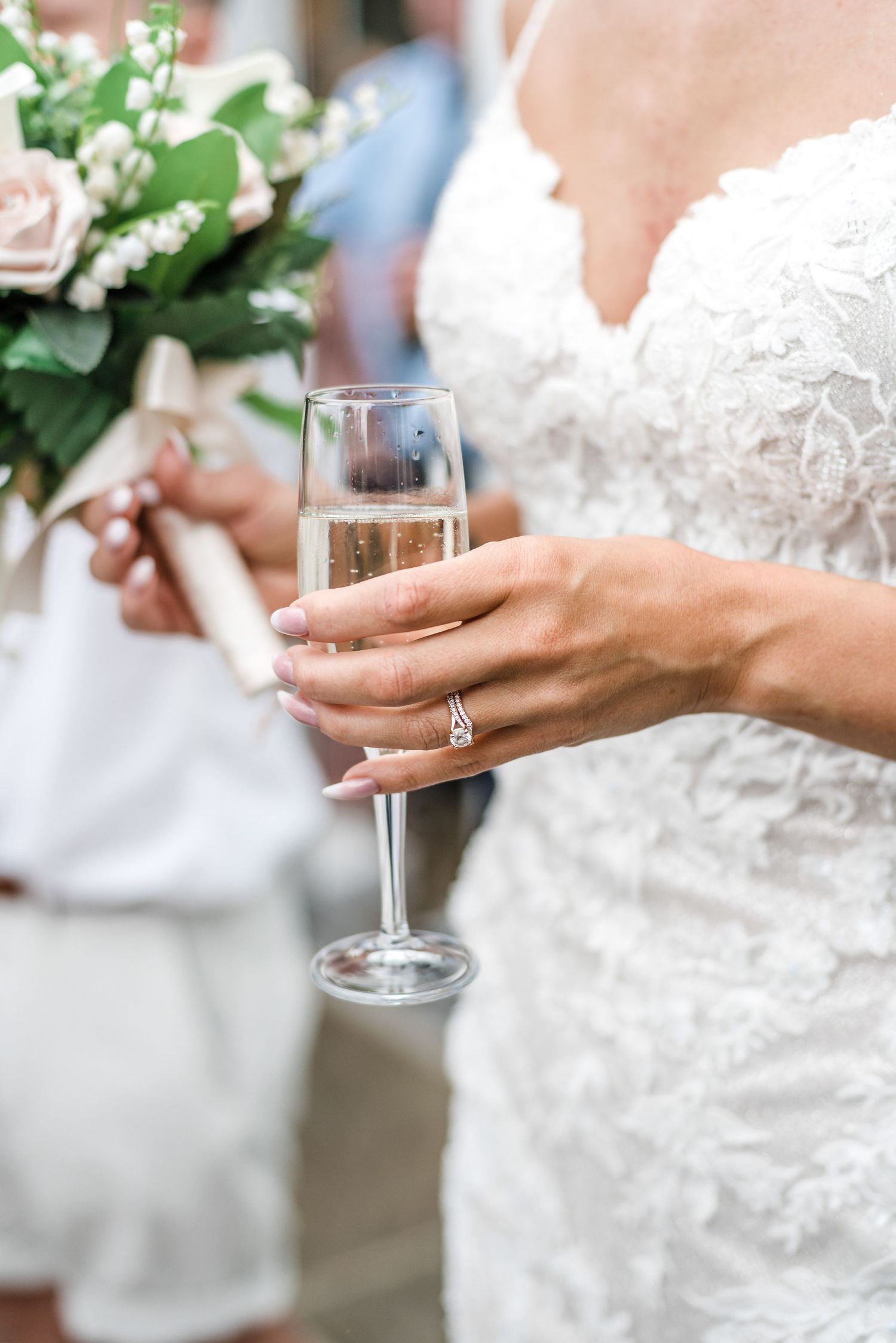Close up of champagne glass and wedding ring details with lace dress and floral bouquet.