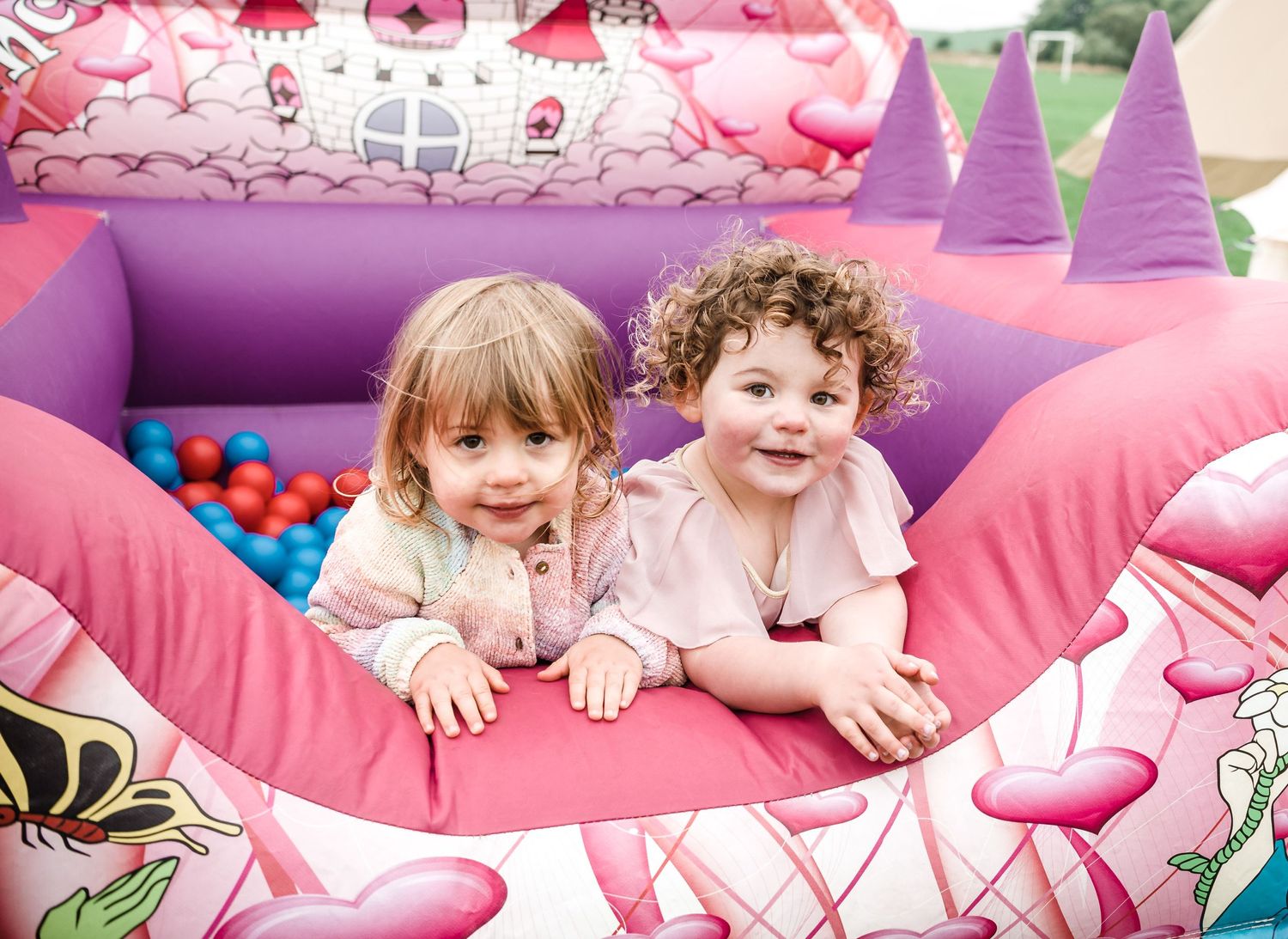 Two young children playing in a pink bounce house filled with balls.