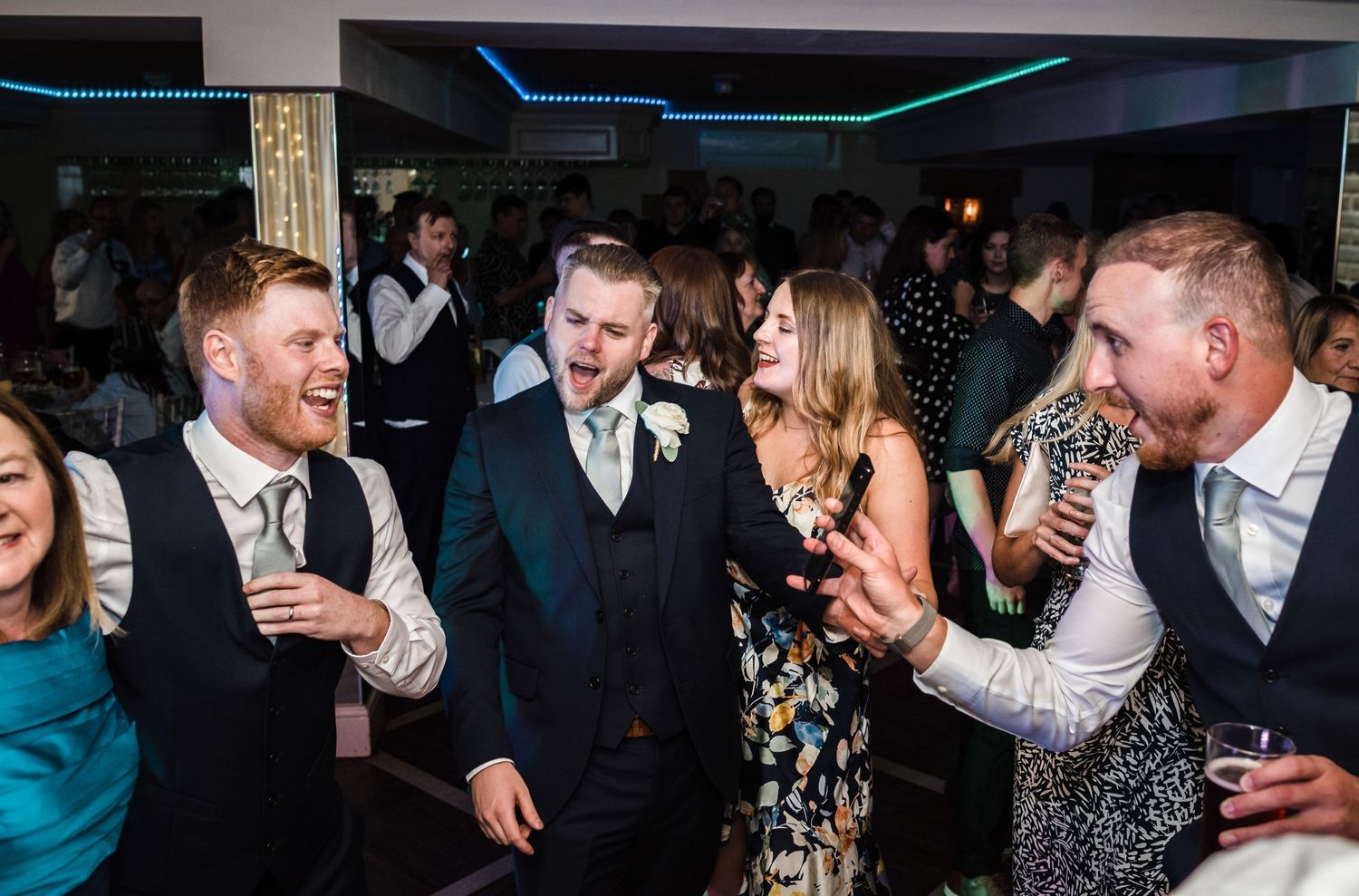 Wedding guests laughing and celebrating during the reception party with colorful lights overhead.
