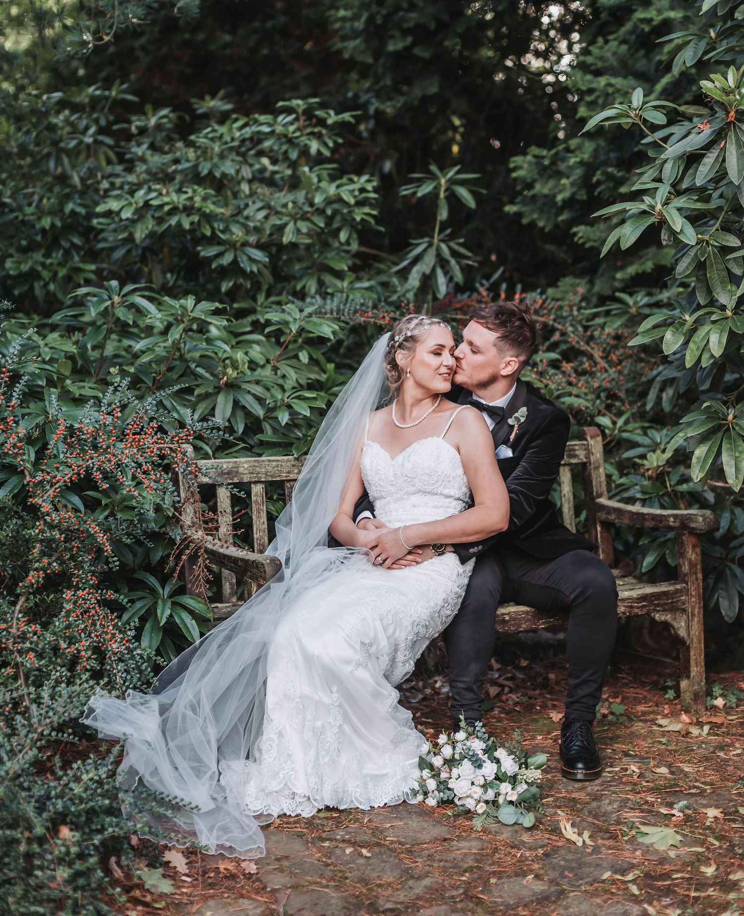 Romantic wedding portrait of couple sharing an intimate moment on rustic wooden bench.