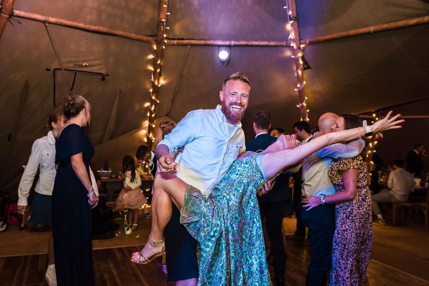 Wedding guests dancing energetically under string lights in a tent venue.