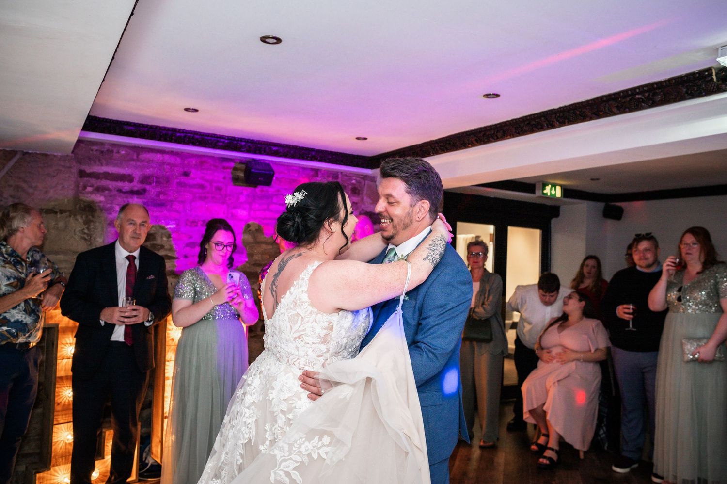 A couple shares their first dance under purple lighting at their wedding reception.