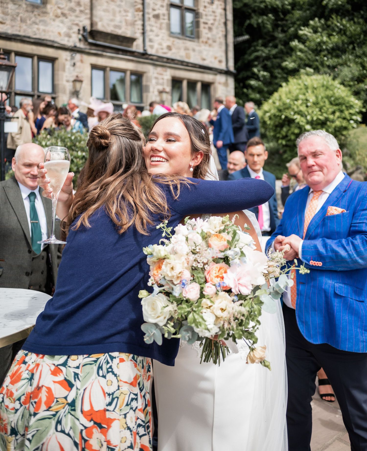 A celebratory wedding moment outdoors with elegant florals and guests wearing formal attire gathering near a stone building.