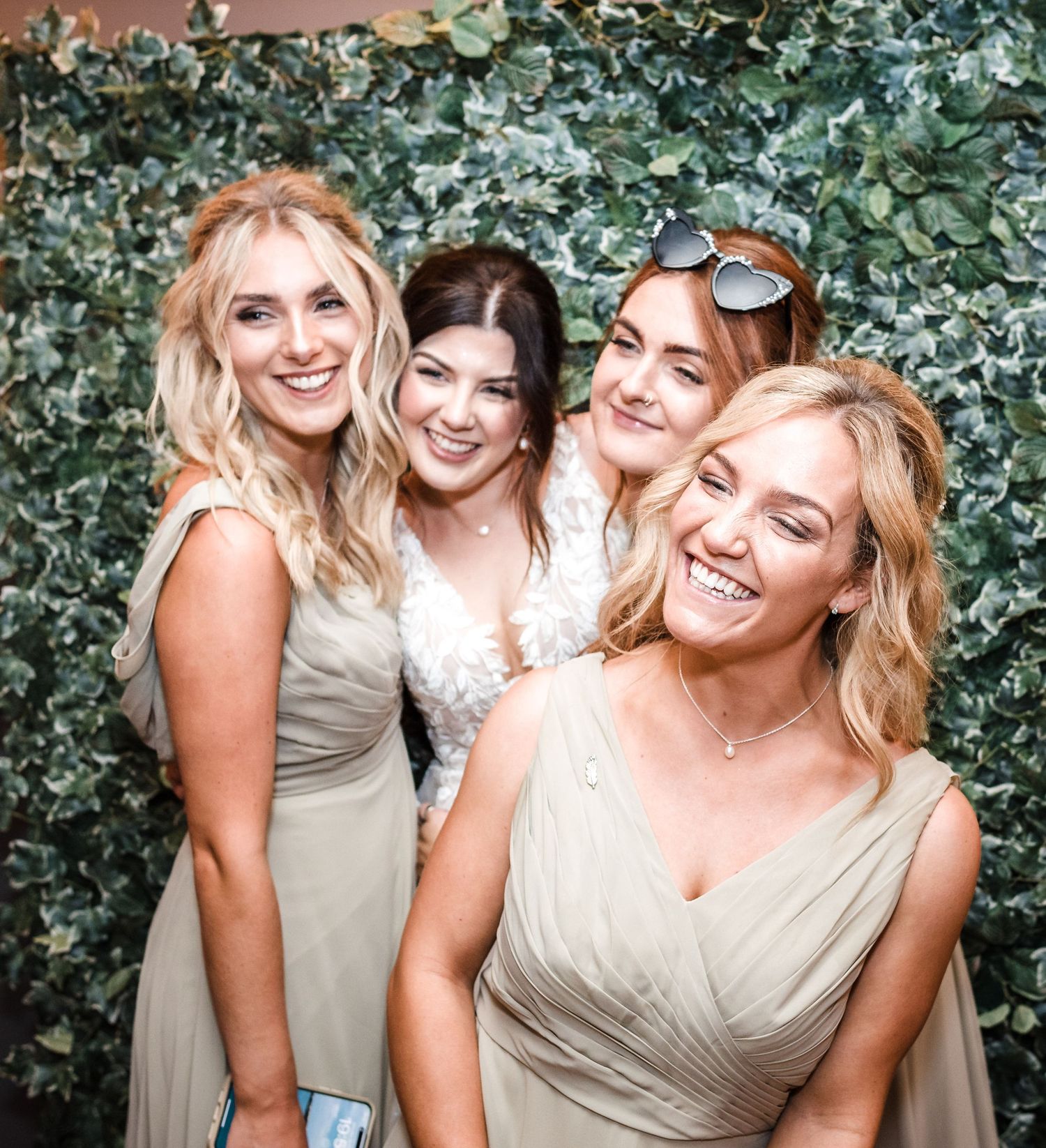 Bridal party in neutral dresses posing against ivy wall backdrop at wedding.